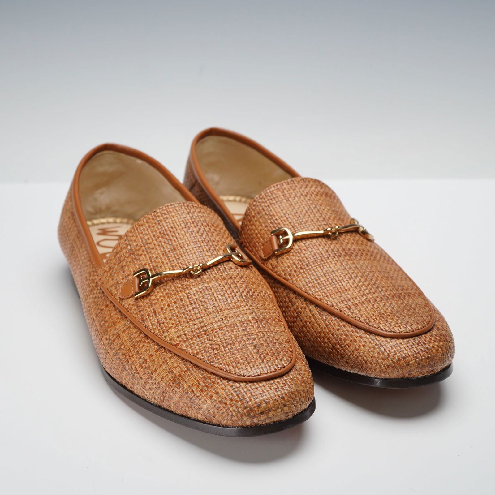 A Pair of Sam Edelman Loraine Brown Loafers: A pair of women's Sam Edelman Loraine loafers featuring woven tan uppers with smooth tan leather trim. Each shoe is finished with gold tone horsebit hardware at the vamp. The interiors have leather fo