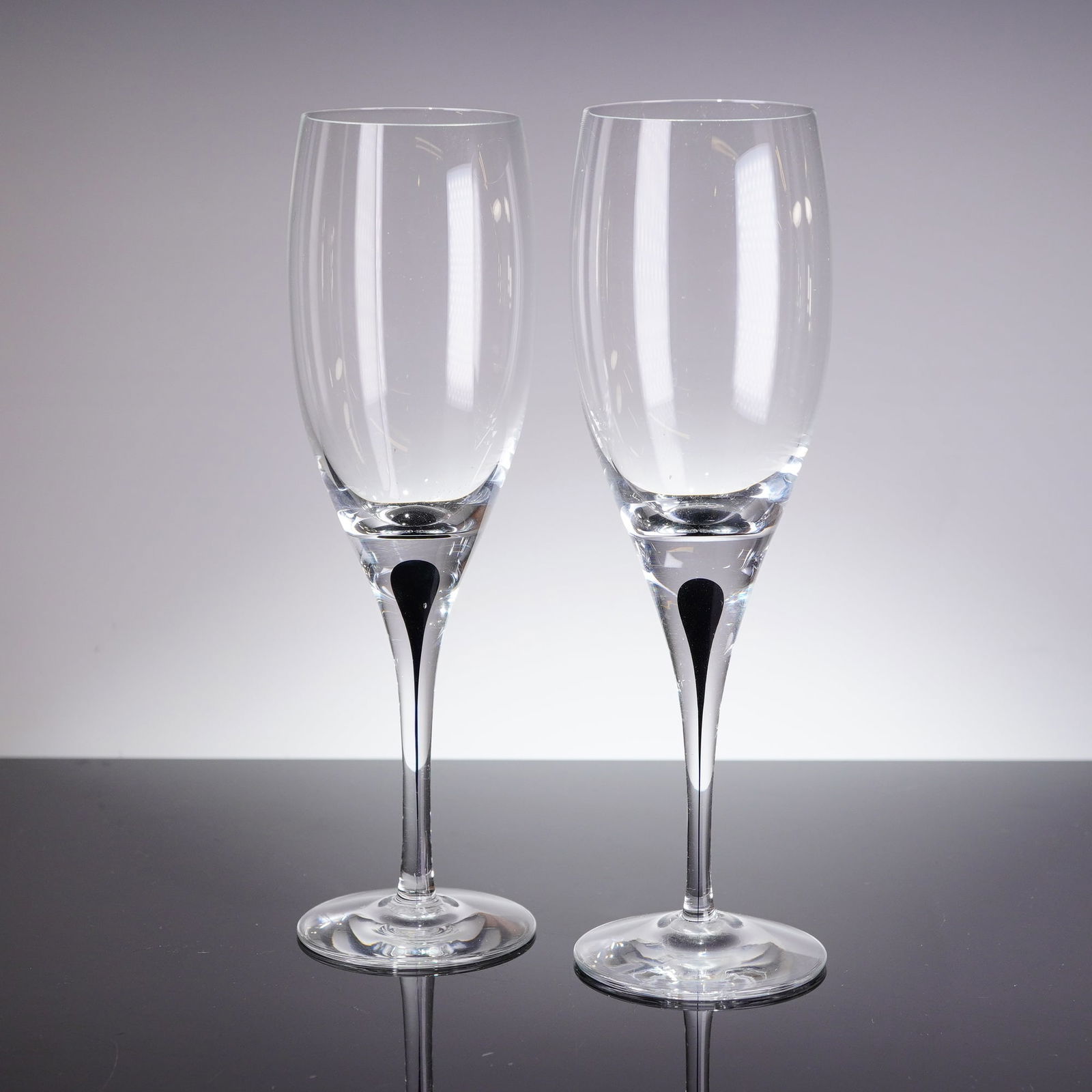 A Pair of Orrefors Intermezzo Black White Wine Glasses by Erika Lagerbielke: A pair of modern white wine glasses atributed to Orrefors, part of the Intermezzo Black series designed by Erika Lagerbielke. Each glass is constructed from clear colorless glass, featuring a tall, tu