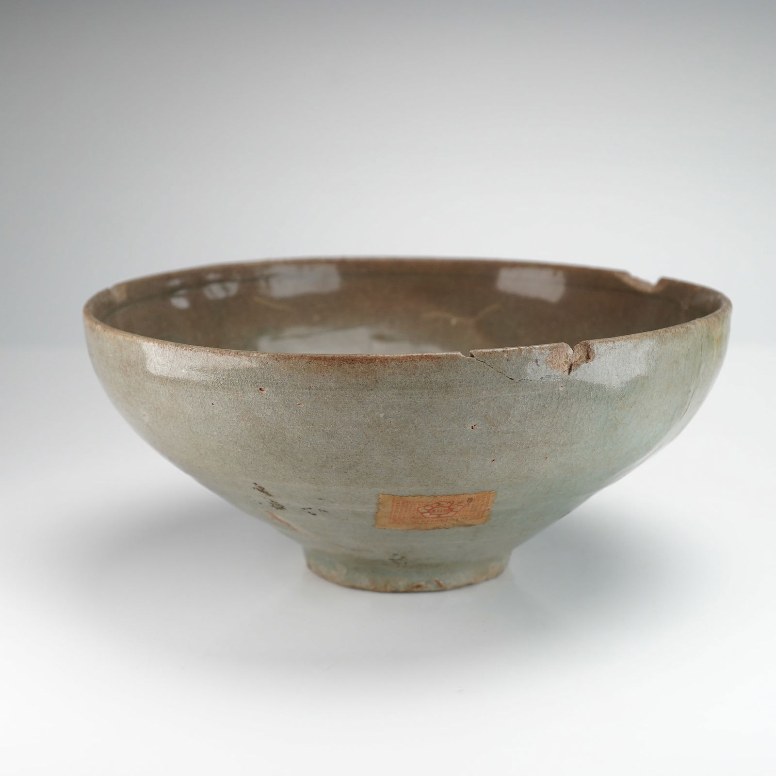 A Korean Celadon Glazed Bowl with Slip Inlay Bird Design: A deep ceramic bowl, covered entirely in a thick, crackled gray-green celadon glaze. The form features steep, curving walls terminating in a slightly everted rim. The interior surface exhibits incised