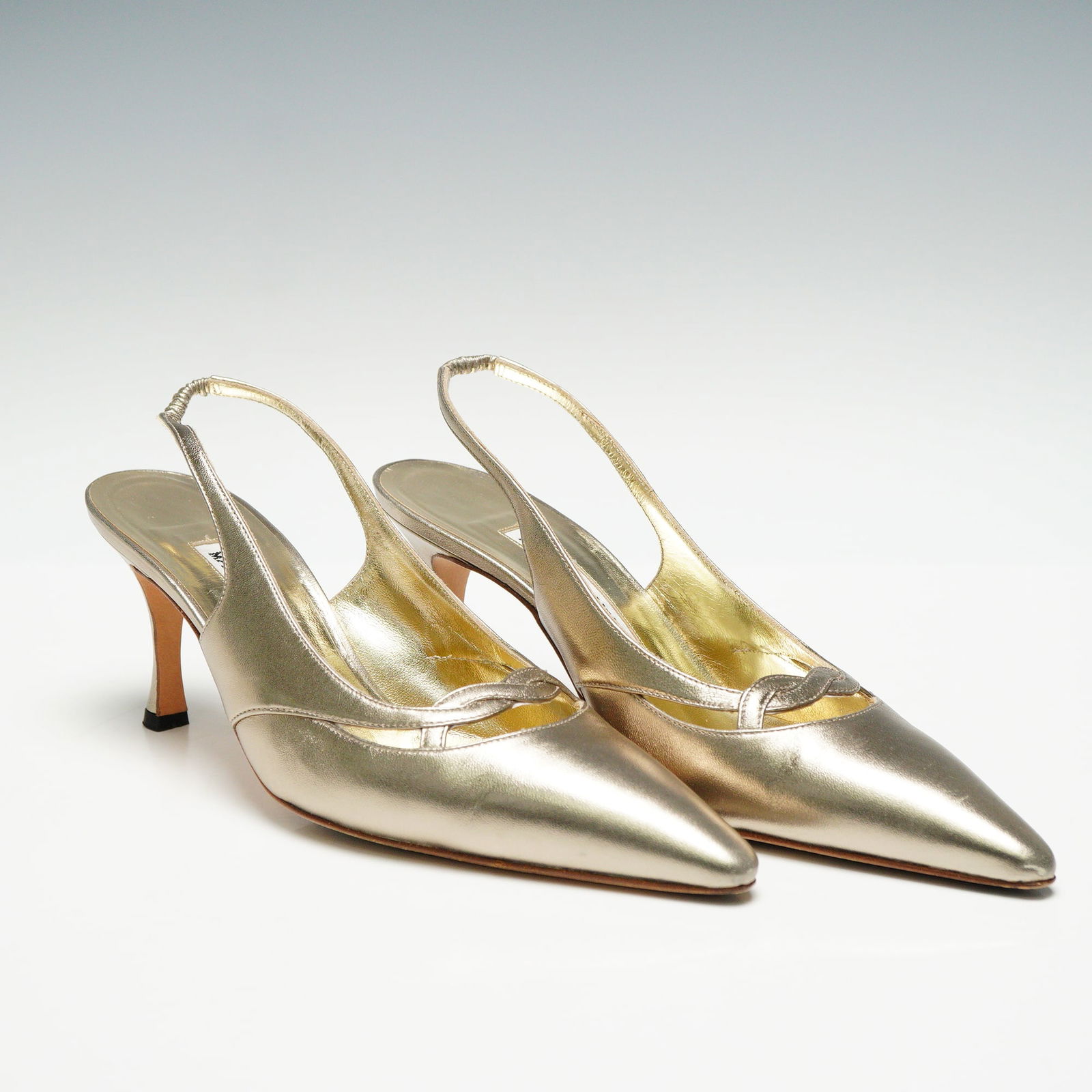 Manolo Blahnik Metallic Leather Slingback Heels: A pair of Manolo Blahnik metallic gold or champagne toned leather slingback heels with pointed toes and a mid height tapered heel. The shoes have silver toned interior lining and natural leather soles