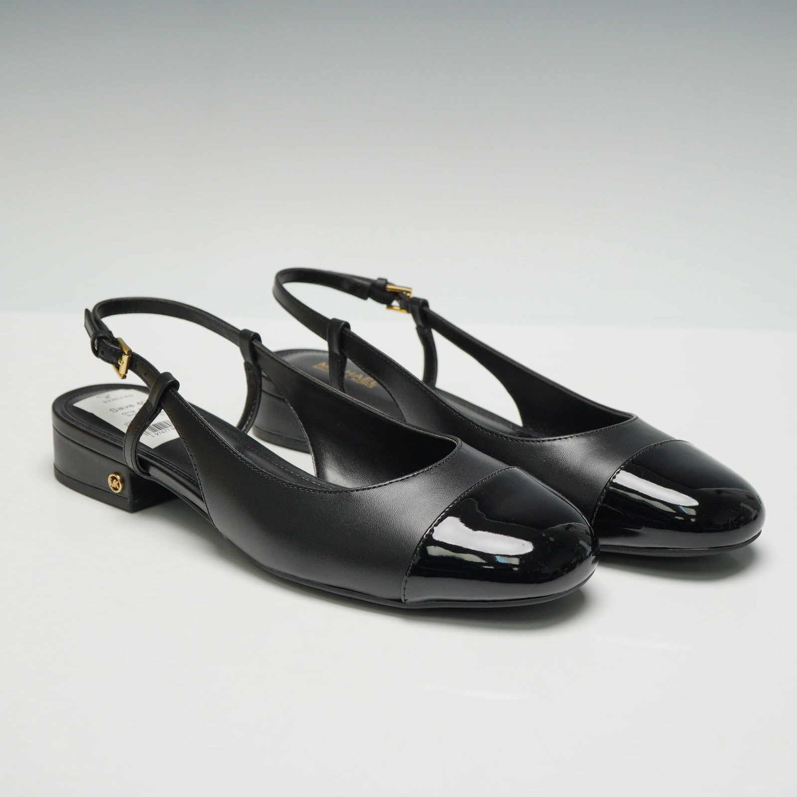 A Pair of Michael Kors Perla Flex Slingback Flats: A pair of womens Perla Flex slingback flats by Michael Kors in black leather with patent cap toes and low block heels. The adjustable straps have gold tone buckles and MK logo hardware at the outer he