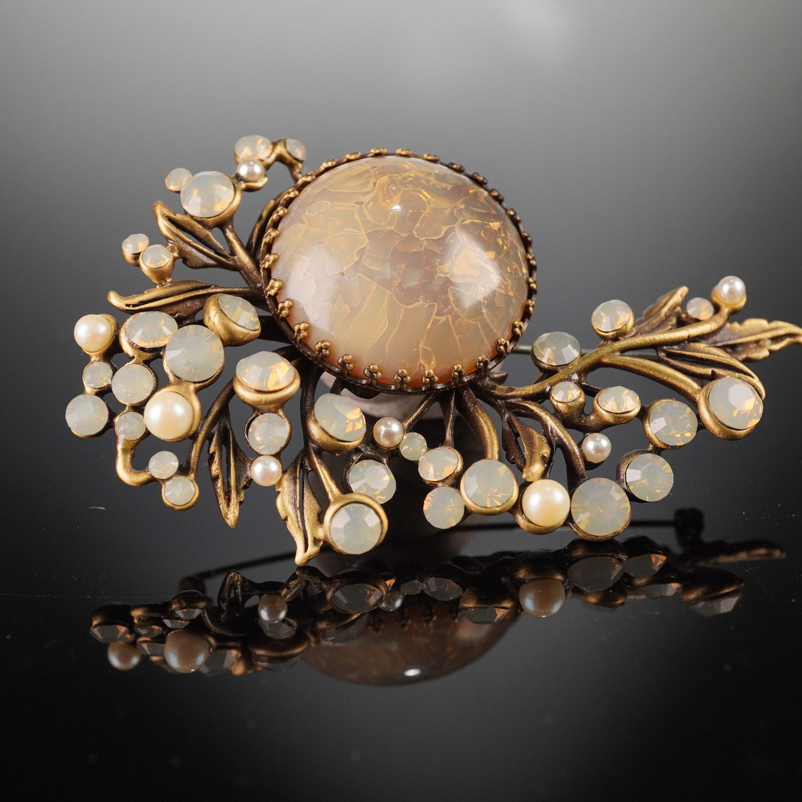 Giorgio Armani Gilt Metal and Opalescent Glass Floral Brooch: Giorgio Armani brooch designed as an organic floral spray, executed in gilt metal with a sculptural openwork form, centered by a large domed opalescent glass cabochon displaying warm honeyed tones and