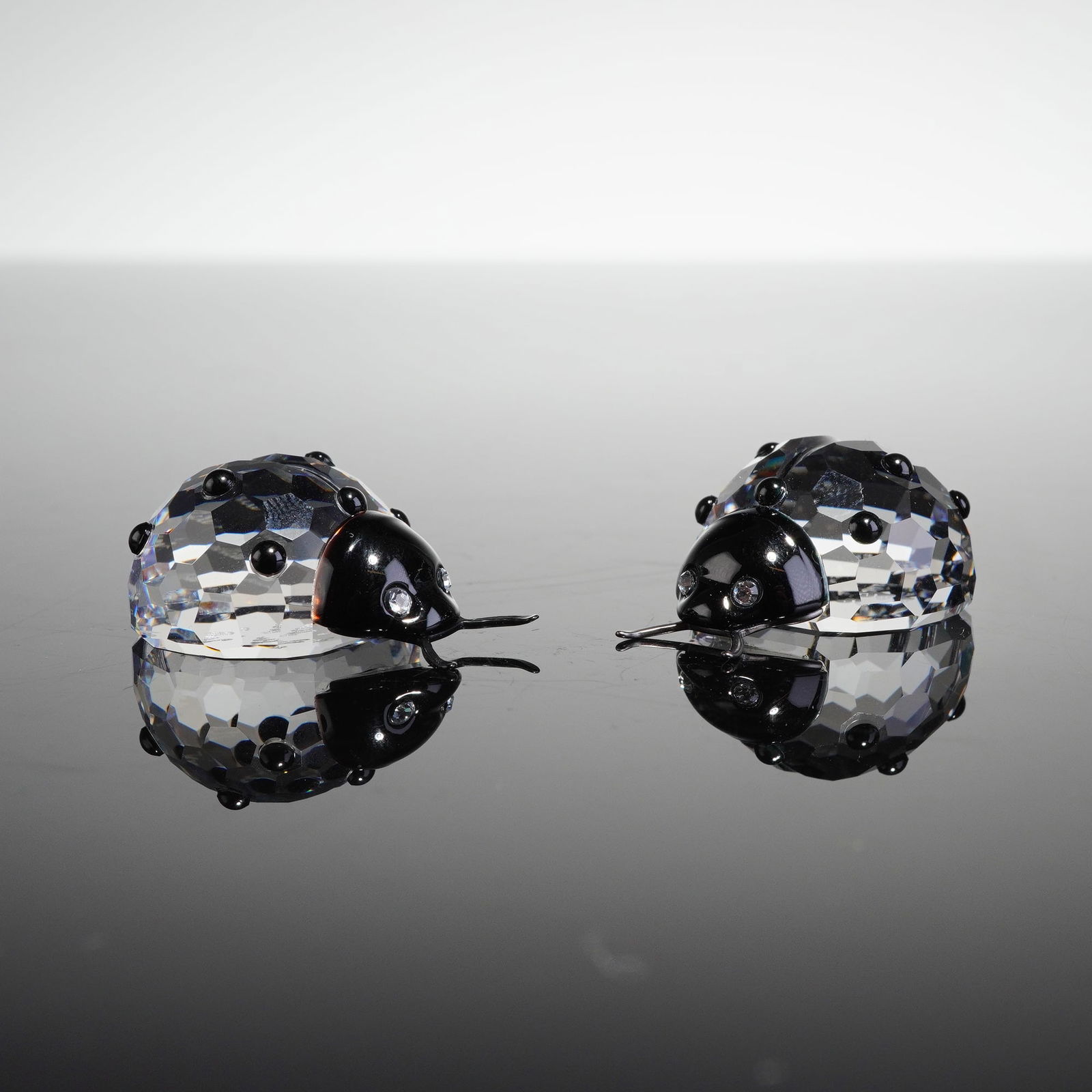 2pc Swarovski Crystal Ladybug Figurines: Group of two decorative figurines crafted by Swarovski, styled as ladybugs. Each figurine is constructed from colorless, faceted crystal forming the body, complemented by a smooth black head and small