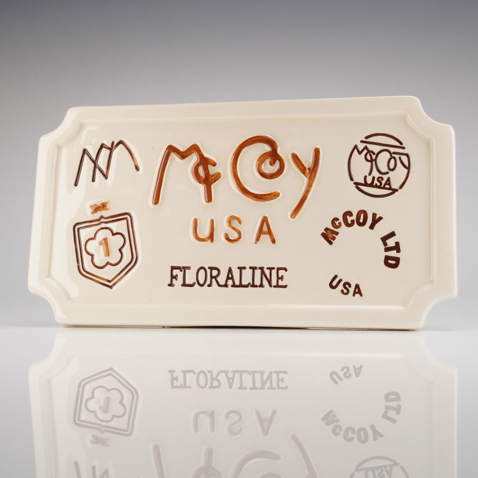 McCoy Pottery Floraline Dealer Display Sign Plaque: A single McCoy Porcelain Display-Trade Sign, executed as a rectangular ceramic plaque with clipped corners, designed to function as a standing dealer advertising sign. The plaque is finished in a glos