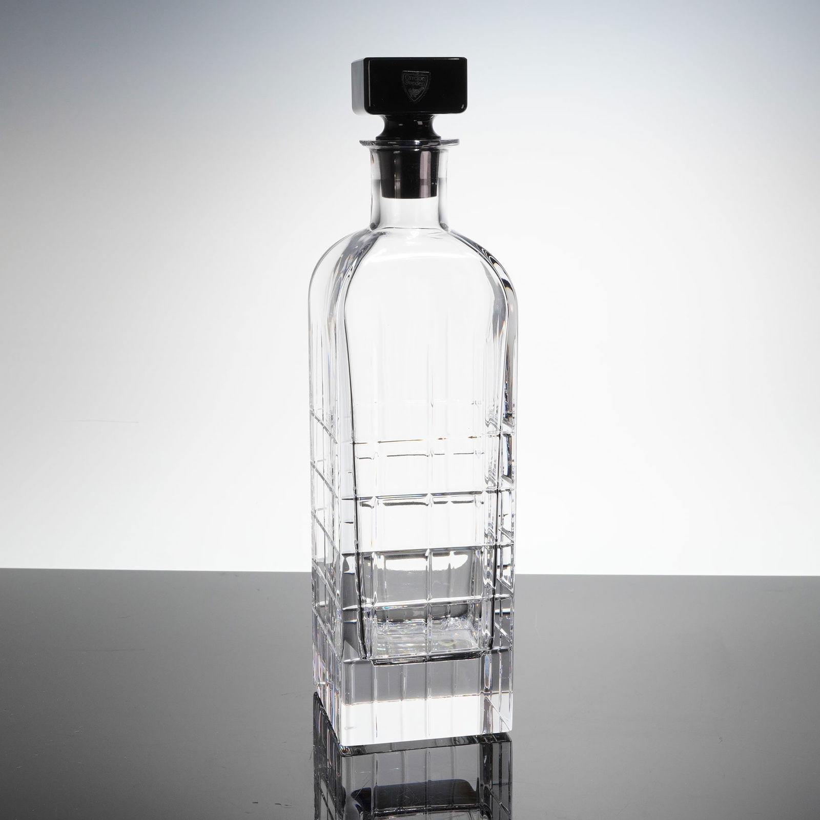 Orrefors by Jan Johansson Street Crystal Decanter with Stopper and Box: A trio of items comprising the Orrefors Street Decanter, its accompanying stopper, and a dark grey presentation box. The decanter is constructed of clear, cut crystal or heavy glass, featuring a tall,