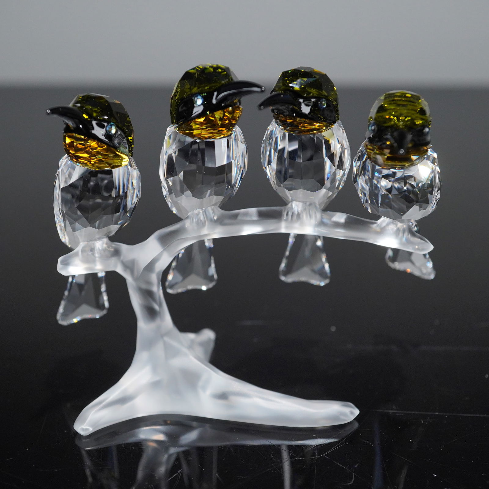 Swarovski Crystal Figurine Bee-Eaters: A Swarovski Crystal Figurine, titled Bee-Eaters. The sculpture depicts four bee-eater birds perched closely together on a branch structure. The birds' bodies and tails are executed in faceted clear, c