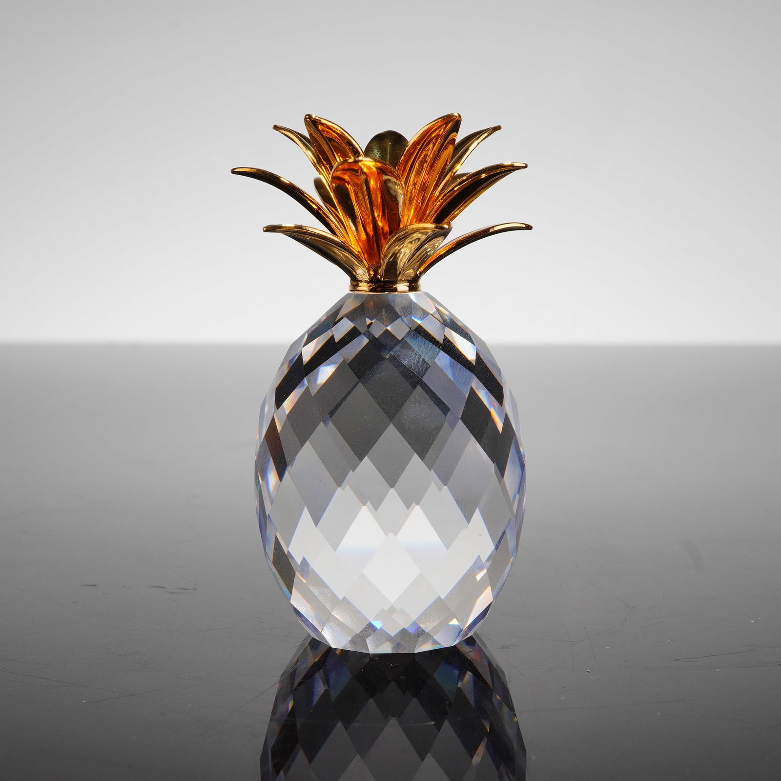 Swarovski Crystal Figurine, Small Pineapple 012726: The body of the figurine is constructed from clear, highly faceted cut crystal, designed to replicate the texture of the fruit. The top is mounted with a stylized crown of bright, reflective gold-tone