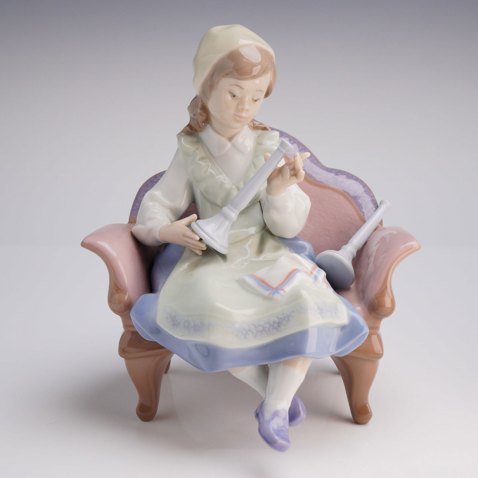 Lladro Porcelain Figurine, Preparing for the Sabbath 1006183: A single glazed Lladro Porcelain Figurine, titled "Preparing for the Sabbath" (Model 6183). The piece depicts a young girl seated in an ornate, padded armchair, meticulously examining components of a