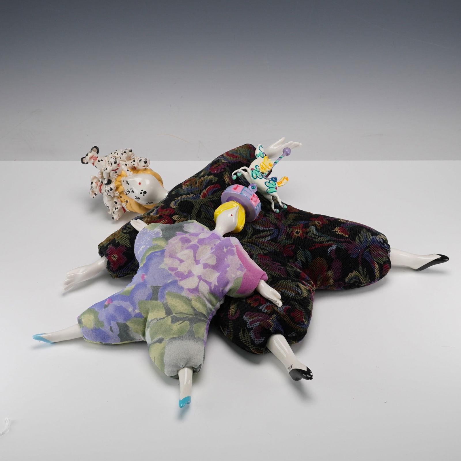 2pc Poupee Millet by Serge Art Dolls: One doll wears a purple and green floral fabric outfit with a yellow hat and blue-tipped feet and finished with carousel horse. The other is dressed in a dark multi-colored floral fabric outfit with