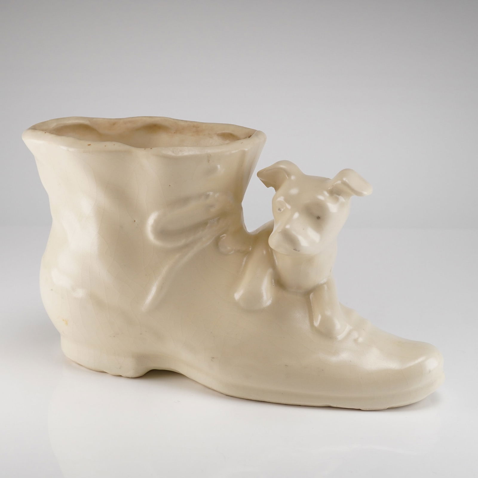 Vintage Shawnee Pottery Dog on Boot Planter, Cream Glaze: This is a single ceramic novelty container, identified as a Vintage Shawnee Dog on Boot Planter. The piece is molded in the form of a high-top boot, finished in an off-white or cream-colored glossy
