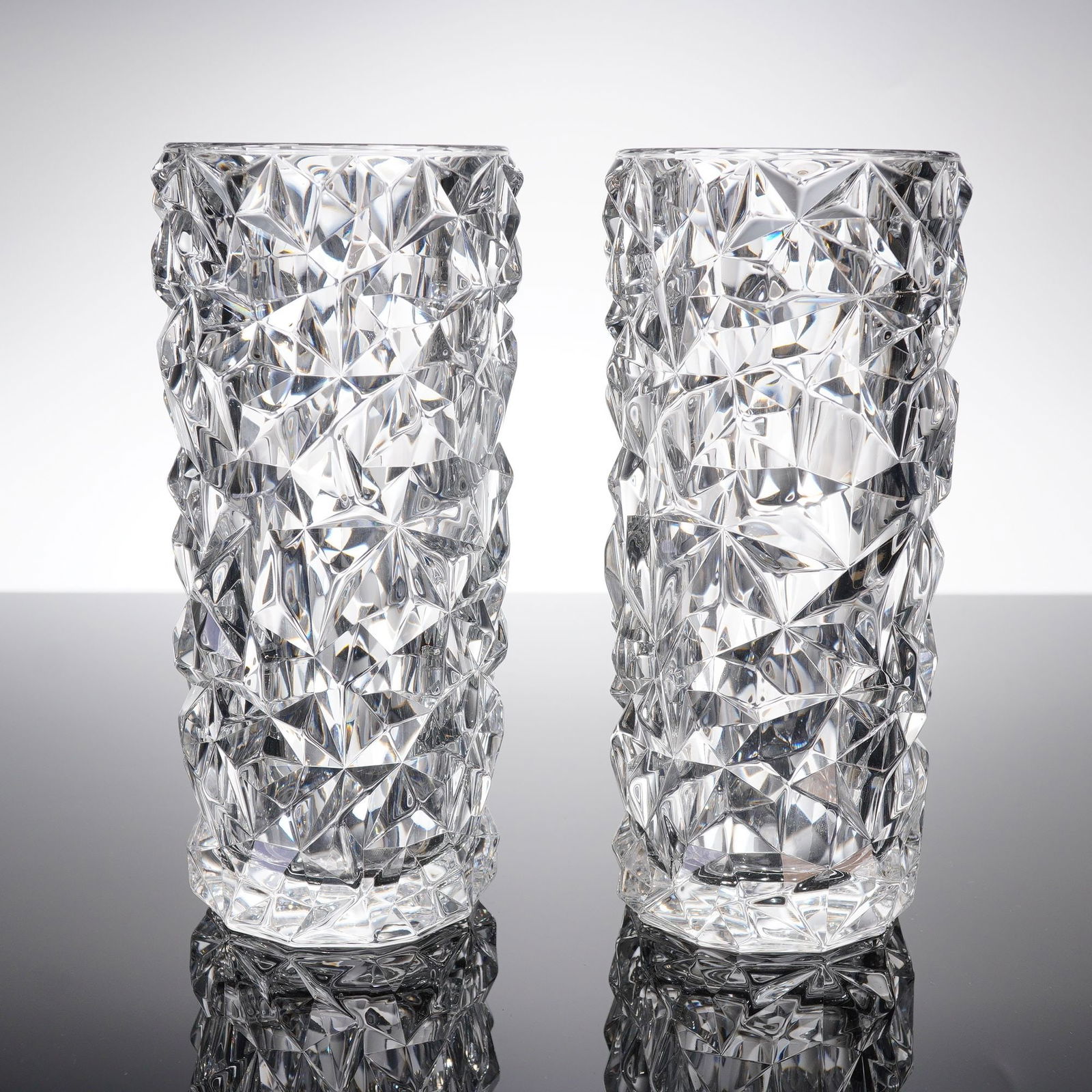 Pair of Orrefors Carat Crystal Vases: A pair of Orrefors crystal vases, identified by the consensus patern name Carat, designed by Lena Bergstrom. These 2pc Orrefor crystal vases are crafted from clear, colorless crystal glass with thick