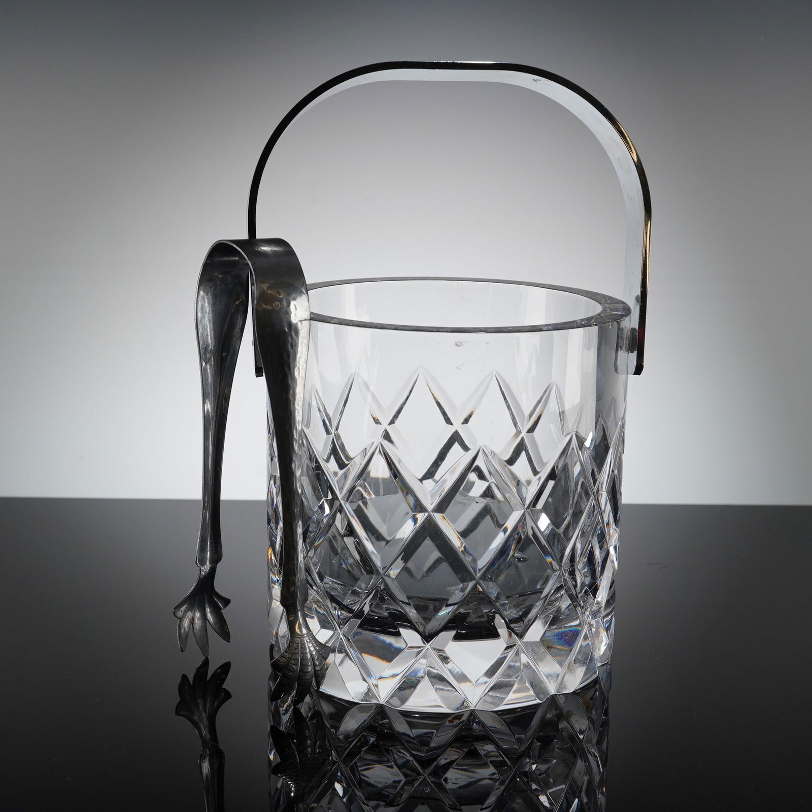 Orrefors Crystal Ice Bucket with Tongs and Drip Stand: A single contemporary ice bucket constructed of clear crystal. The piece is characterized by deep, asymmetric geometric faceting, indicative of a modern design aesthetic. The material is heavy and hig