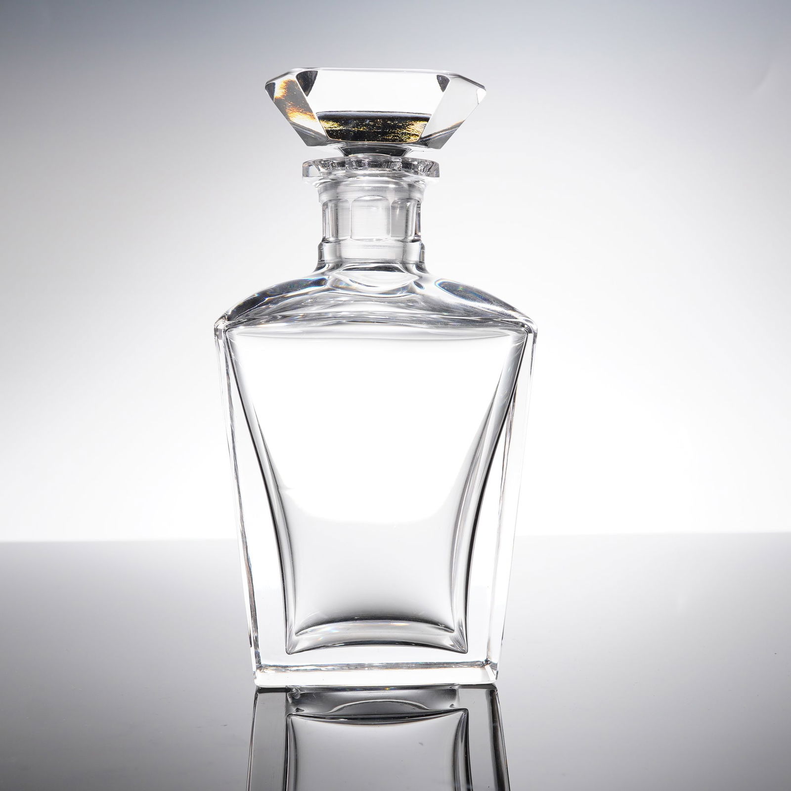 Orrefors Crystal Decanter and Stopper: A contemporary decanter set constructed of heavy, clear crystal. The set comprises a decanter body and a matching faceted stopper. The decanter features a square base and tapered sides leading to defi