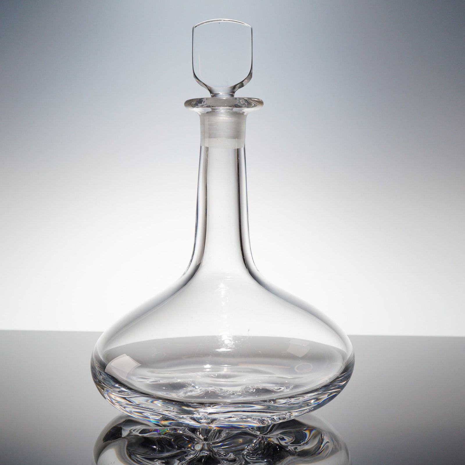 Orrefors Crystal Ships Decanter and Stopper: An Orrefors-style Crystal Ships Decanter and its corresponding ground glass stopper. The vessel features a wide, shallow, bulbous body designed for stability, transitioning to a tall, narrow neck. The