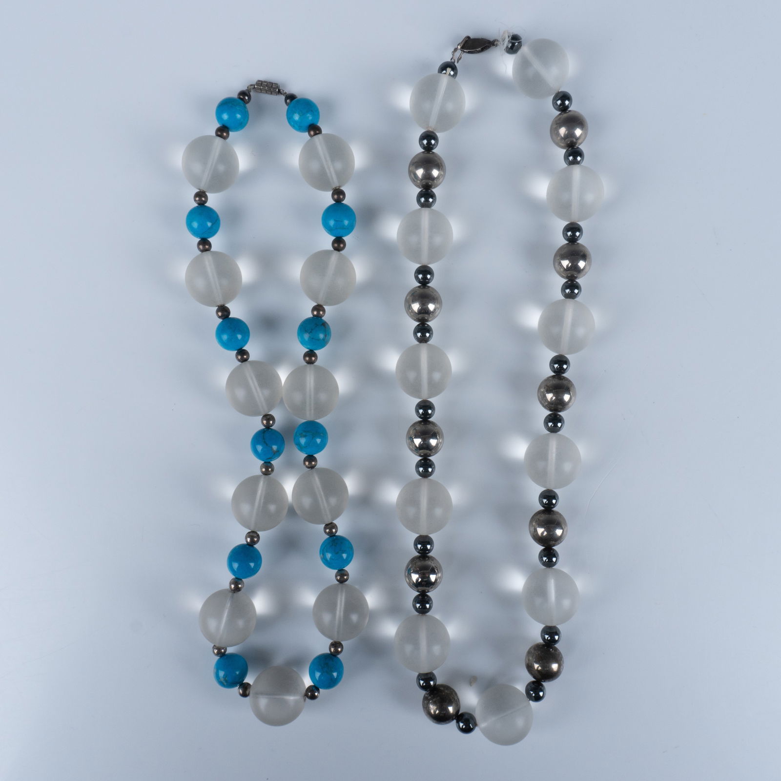 Pair of Opaque White Clear Stone Necklaces: Splendid duo of beaded necklaces that consists of a fish hook clasp necklace with opaque spheres and Navajo silver beads, and a barrel clasp necklace with opaque spheres and turquoise beads. Longest