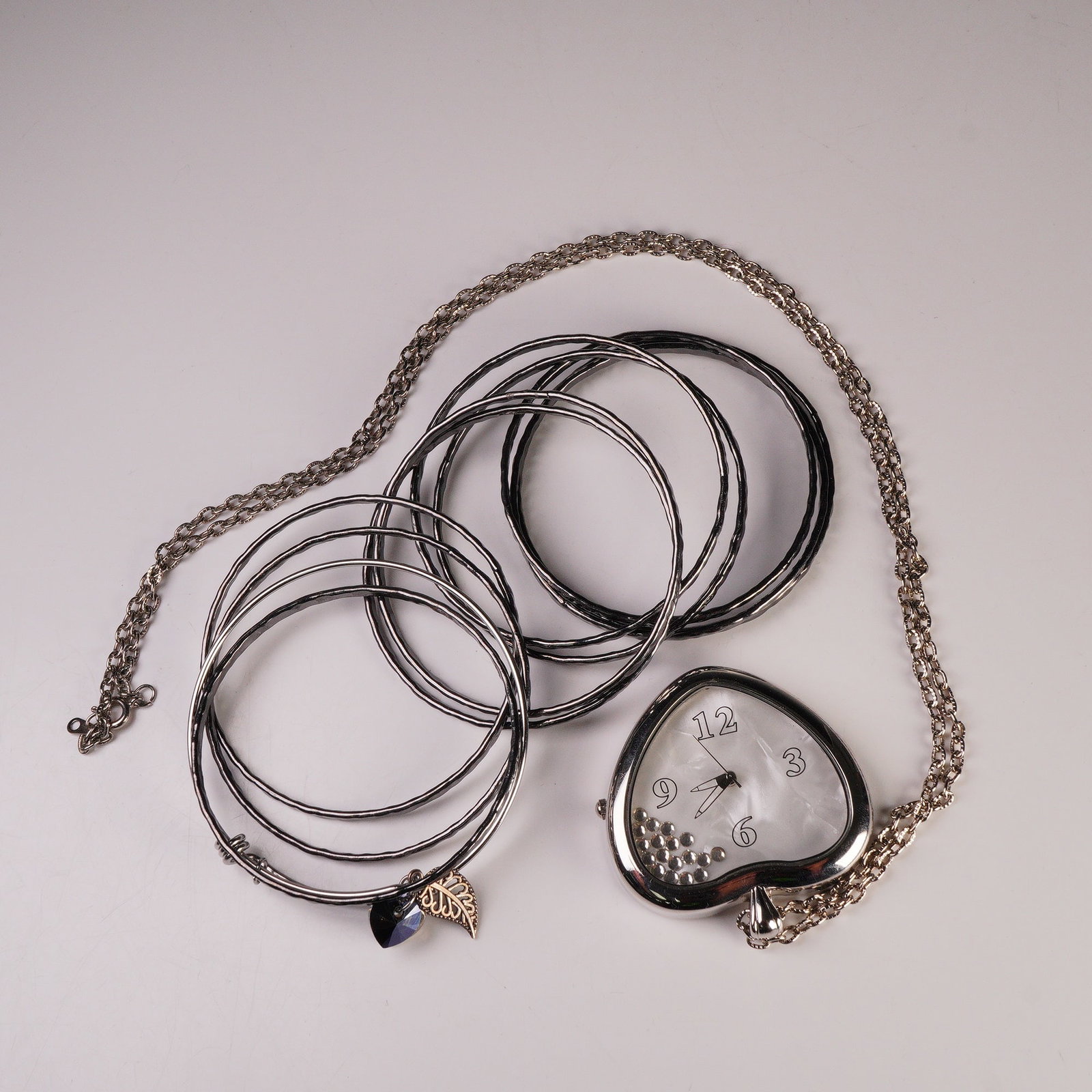 12pc Costume Jewelry, Watch Necklace, Charm Bangle and Gray Metal Bangles: Stylish costume jewelry collection including a mix of contemporary silver-tone accessories. The lot features a heart-shaped pendant watch necklace with a white mother-of-pearl dial and loose