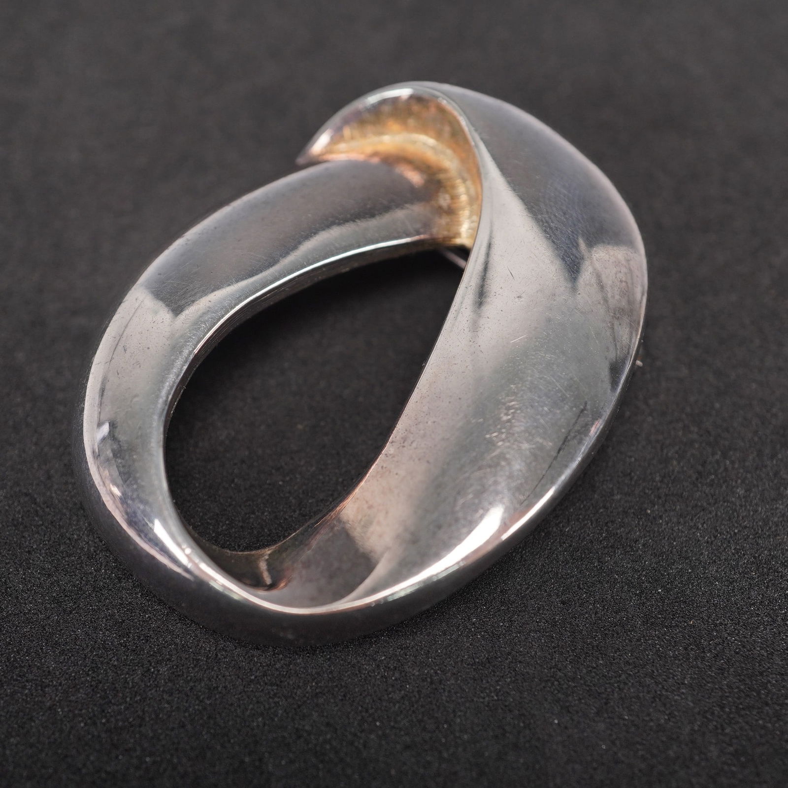 Sculptural Silver Tone Pendant Brooch: Modernist silver brooch in a bold sculptural loop form, featuring a high-polish finish with fluid, asymmetrical curves. The interior surface displays a hammered texture and bears a stamped maker's