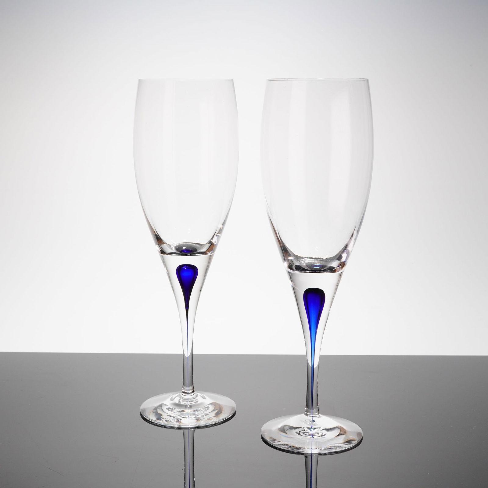 A Pair of Orrefors Intermezzo Blue Champagne Flutes by Erika Lagerbielke: A pair of modern champagne flutes from the Orrefors Intermezzo Blue patern, designed by Erika Lagerbielke. The fi?utes are crafted from clear crystal glass, featuring a tall, narrow bowl suitable for