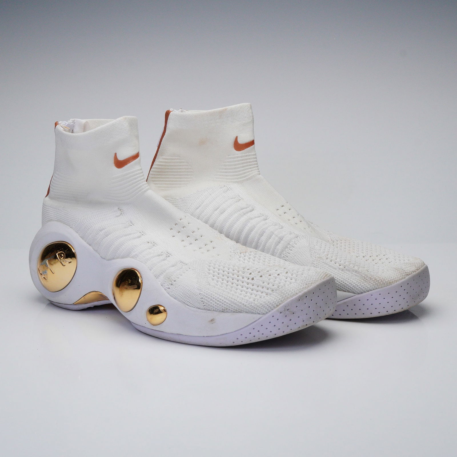 A Pair of Nike Flight Bonafide Rose Gold Sneakers: A pair of Nike Flight Bonafide Rose Gold athletic shoes. These modern high-top athletic shoes feature a white knitted textile, sock-like upper with a rear zipper closure featuring NIKE branded pulls