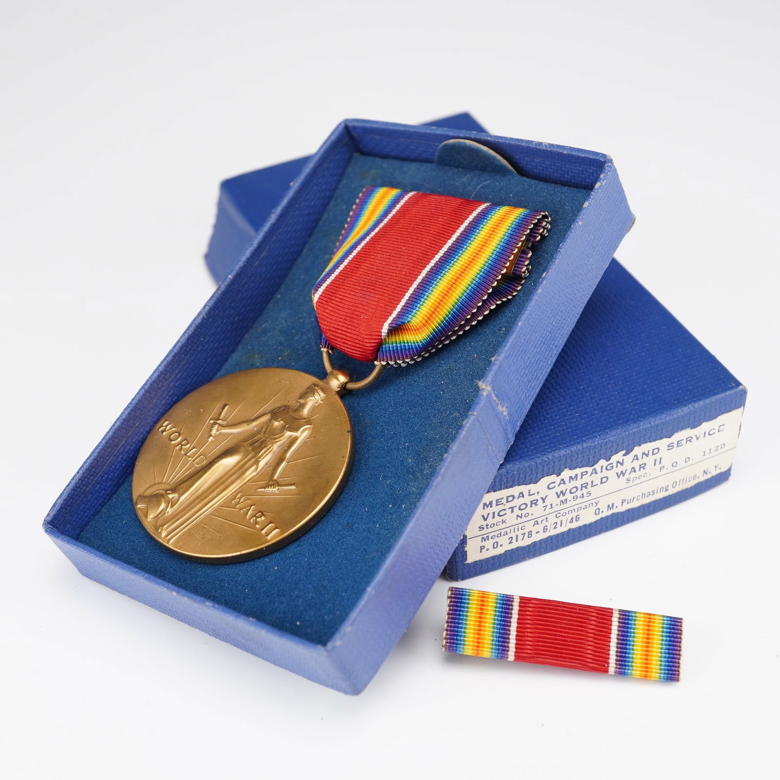 U.S. WWII Victory Medal in Original Box with Service Ribbon: A United States World War II Victory Medal presented in its original blue government-issue box, accompanied by the matching service ribbon. The bronze medal features the standing figure of Liberation