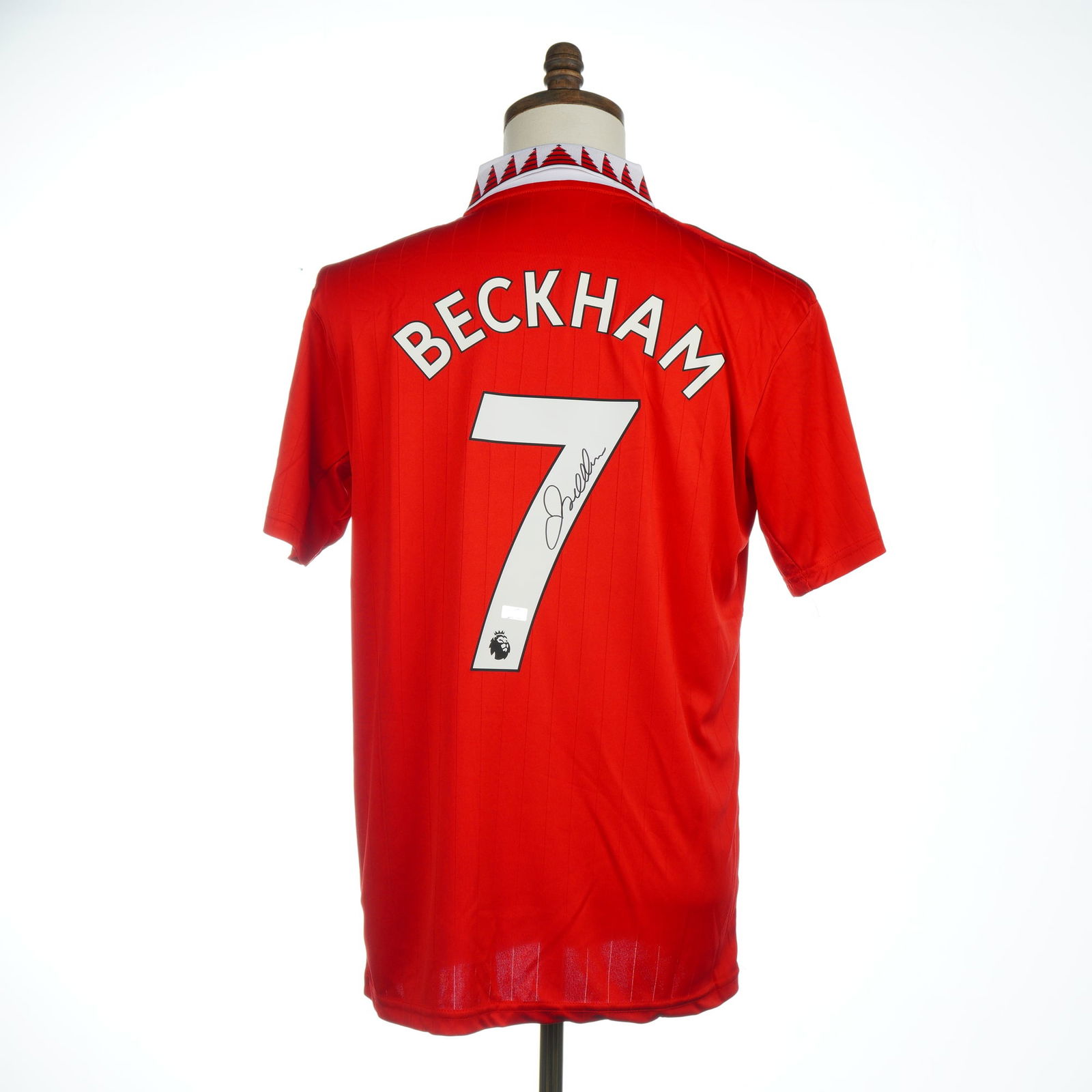 David Beckham Autographed #7 Manchester United 2022-23 Home Jersey with COA: A David Beckham Autographed #7 Manchester United 2022-23 Replica Home Jersey, authenticated by Panini Authentic. The short-sleeved red synthetic shirt, manufactured by Adidas, features subtle