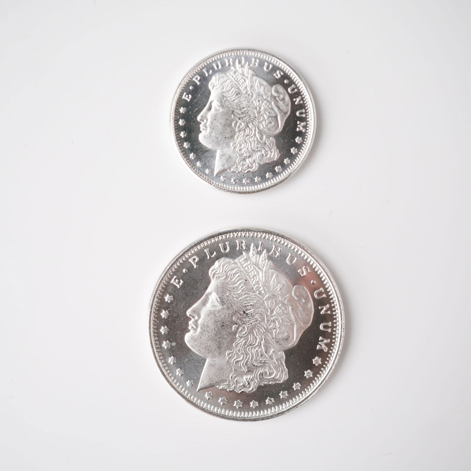 2pc 1/2 Troy Ounce and 1/4 Troy Ounce Morgan Silver Rounds: Two silver replica rounds modeled after the historic Morgan Dollar, each featuring the classical Liberty head on the obverse with the legend E Pluribus Unum encircled by stars. The reverses present