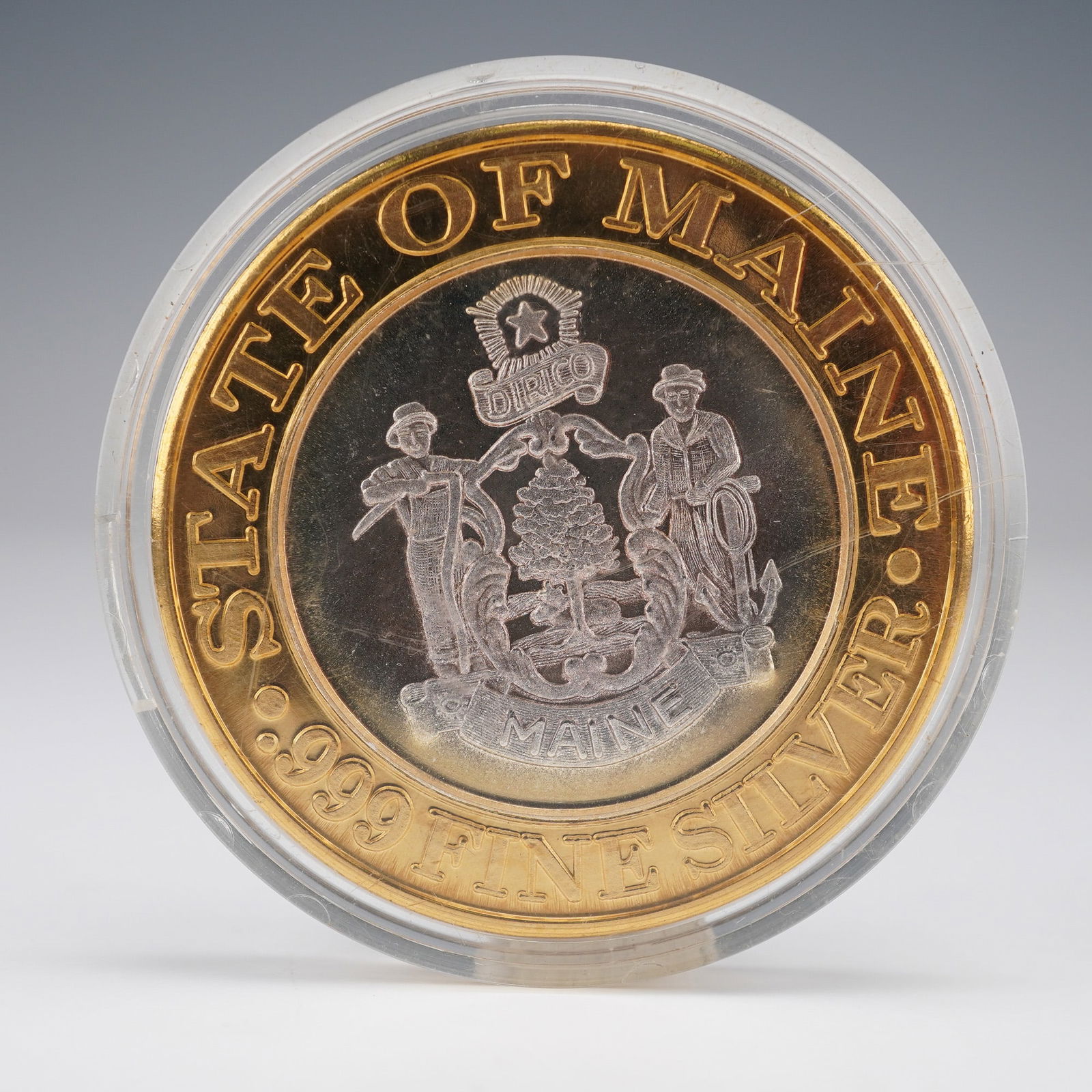 1994 Foxwoods Resort Maine .999 Silver Ten-Dollar Token: The medallion features a silver-toned core encircled by a gold-toned outer ring. The obverse depicts the Seal of Maine, portraying a farmer and seaman flanking a pine tree and moose, surmounted by a