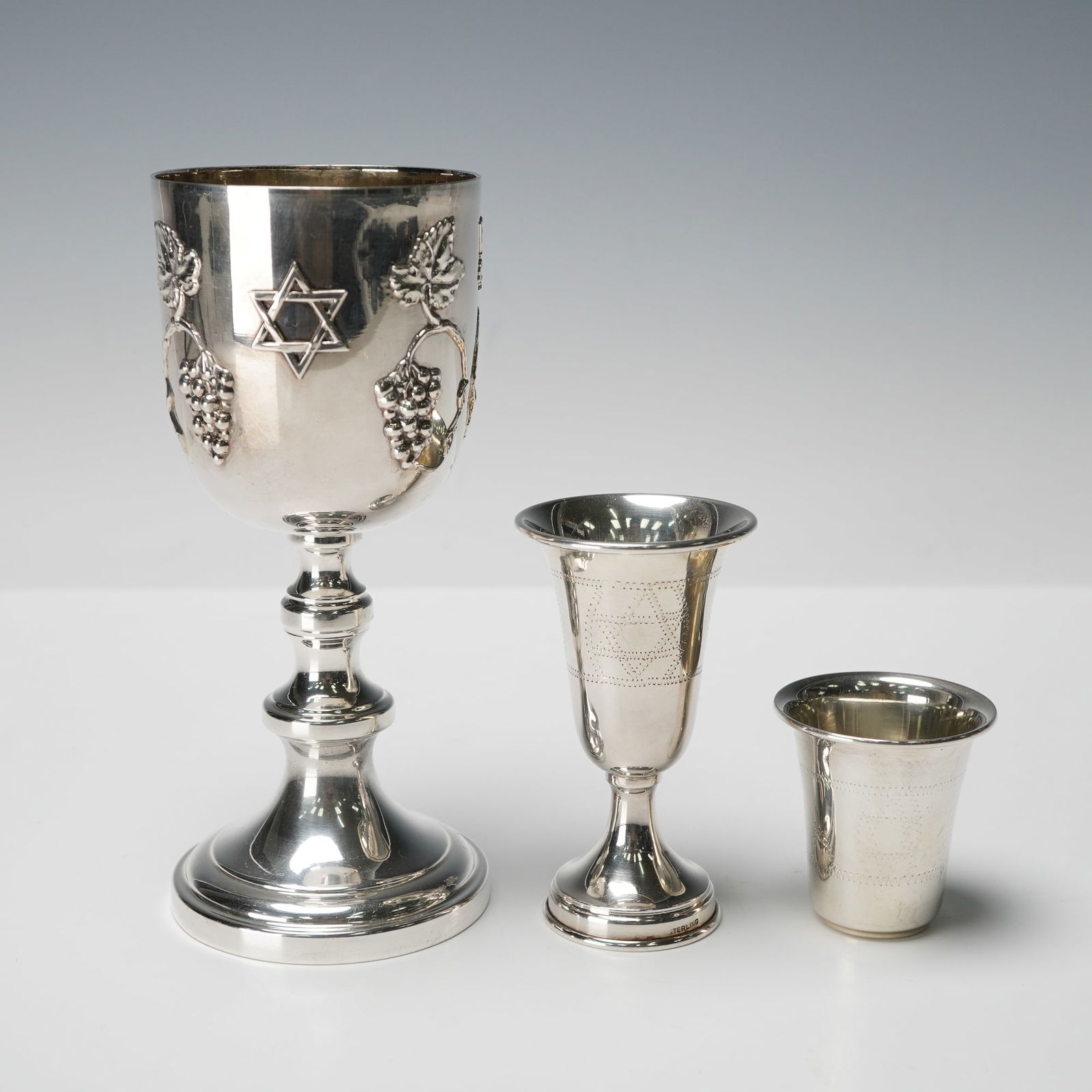 3pc Judaica Sterling Silver Kiddush Cups: Group of three sterling silver Kiddush cups in graduated sizes. The largest cup features raised grapevine decoration, a raised Star of David, and an inscription reading From Mom and Dad June 25 1958.