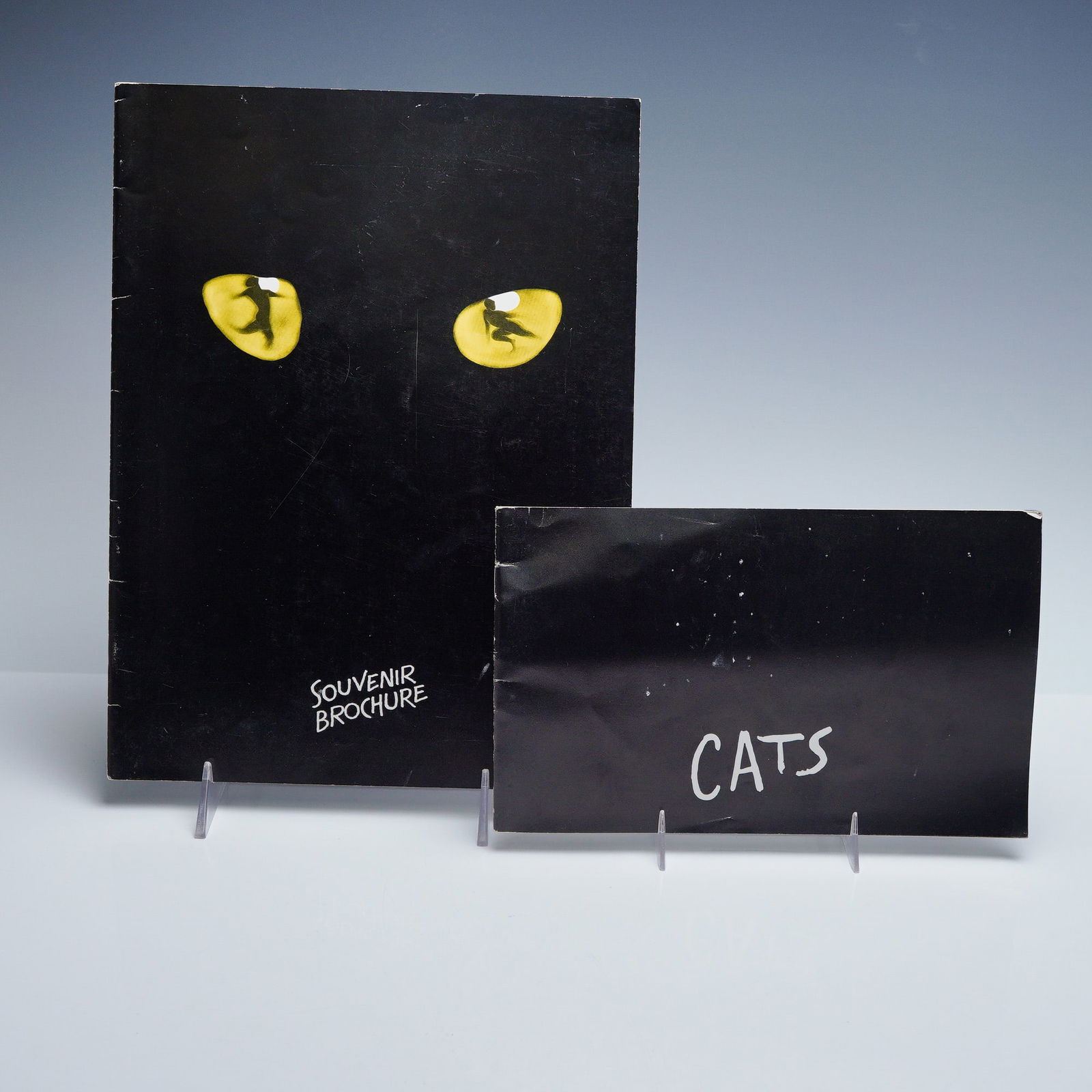 2pc Cats Musical Souvenir Booklets London Theatre Lot: Pair of original Cats musical souvenir booklets from the New London Theatre in Drury Lane. Includes the full-size black cover brochure featuring the iconic yellow cat eyes, and the smaller