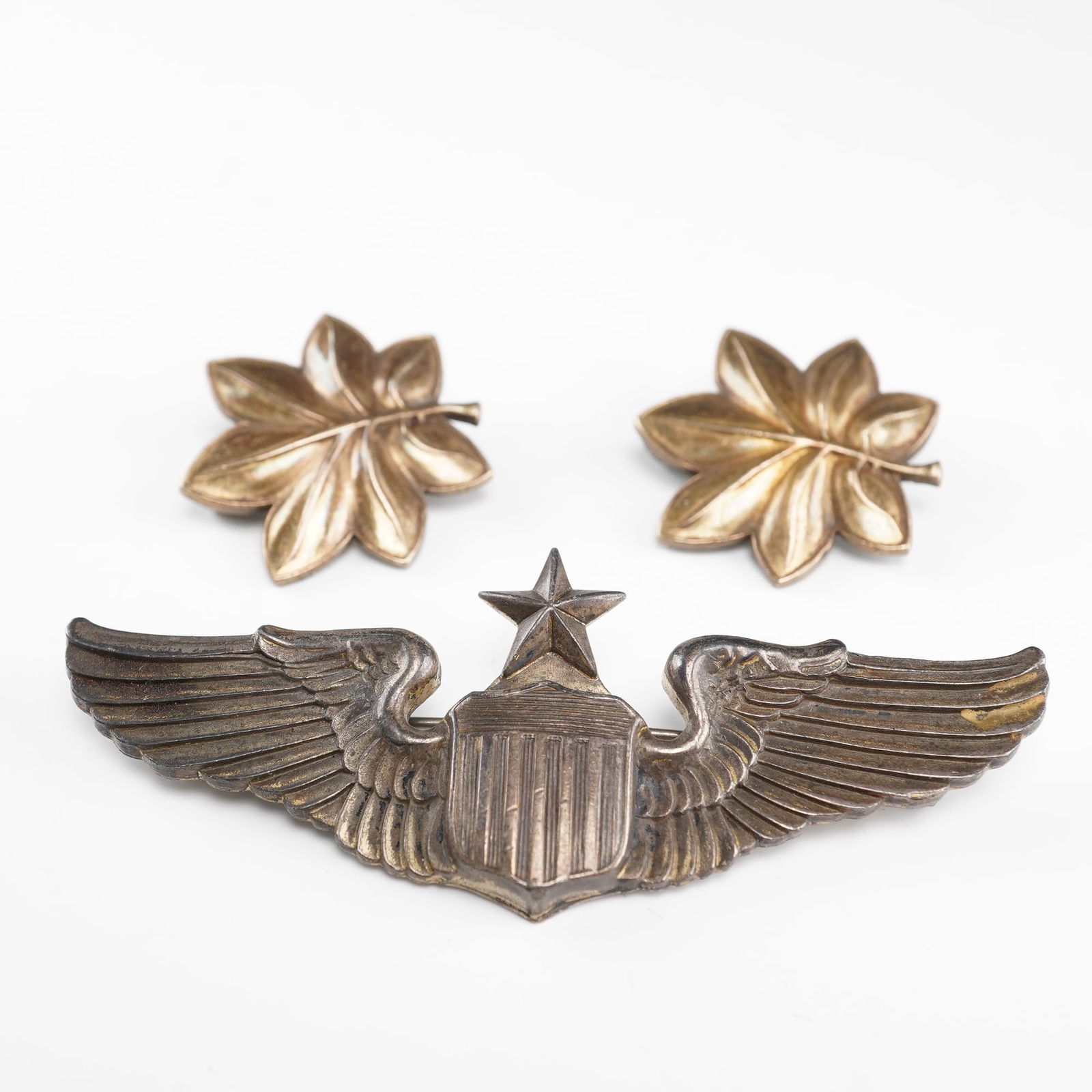 A Trio of WWII Era US Army Air Force Sterling Silver & Gold-Filled Insignia: A trio of miscellaneous sterling silver and gold-filled US Army Air Force insignia, likely dating to the World War II era. The lot includes one large aviation wing insignia and a matched pair of small