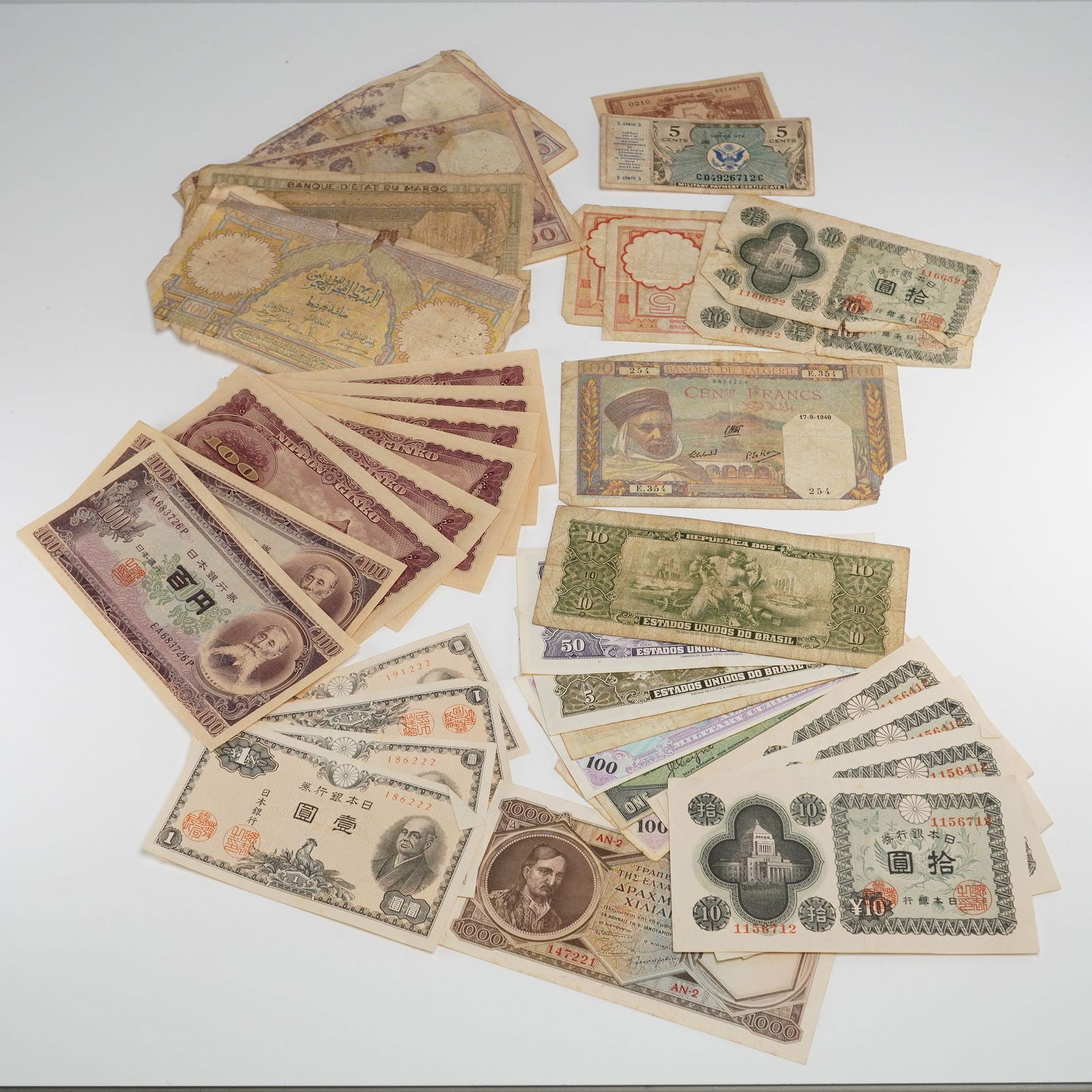 A Collection of Assorted Early to Mid-20th Century World Banknotes: Approx. fifty world banknotes from Japan, Morocco, Algeria, Brazil, Greece, etc. Denominations from 5 cents to 1000. Designs include portraits, architecture, allegorical figures. One Algerian note