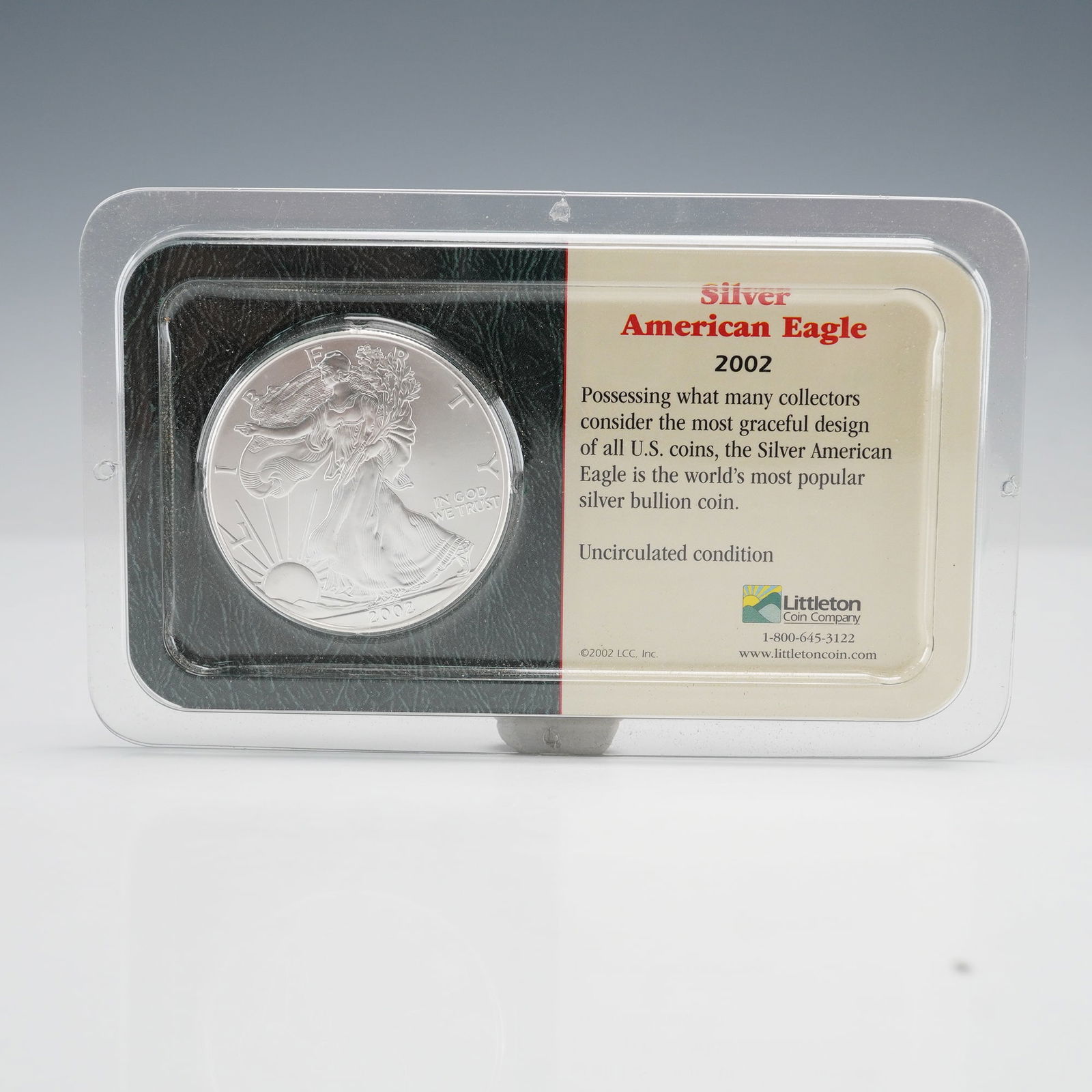 2002 Silver American Eagle by Littleton Coin Co.: A 2002 Silver American Eagle coin in a clear plastic display holder by Littleton Coin Company. Obverse features Liberty Walking design, dated 2002 with IN GOD WE TRUST. Reverse shows Heraldic Eagle