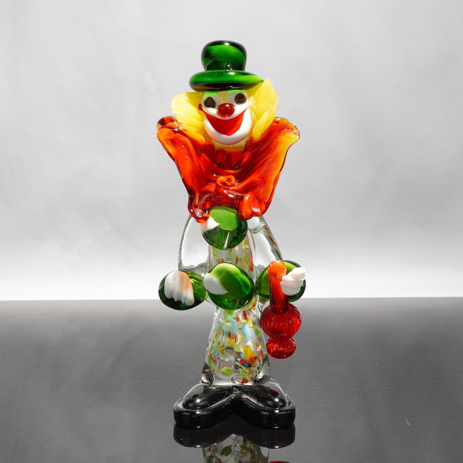 Murano Art Glass Clown Figurine: A Murano blown'glass clown figurine with green top hat, yellow ruffled hair, white face with red nose and smile, red ruffled collar, and a clear body embedded with multi'colored glass specks. Clear