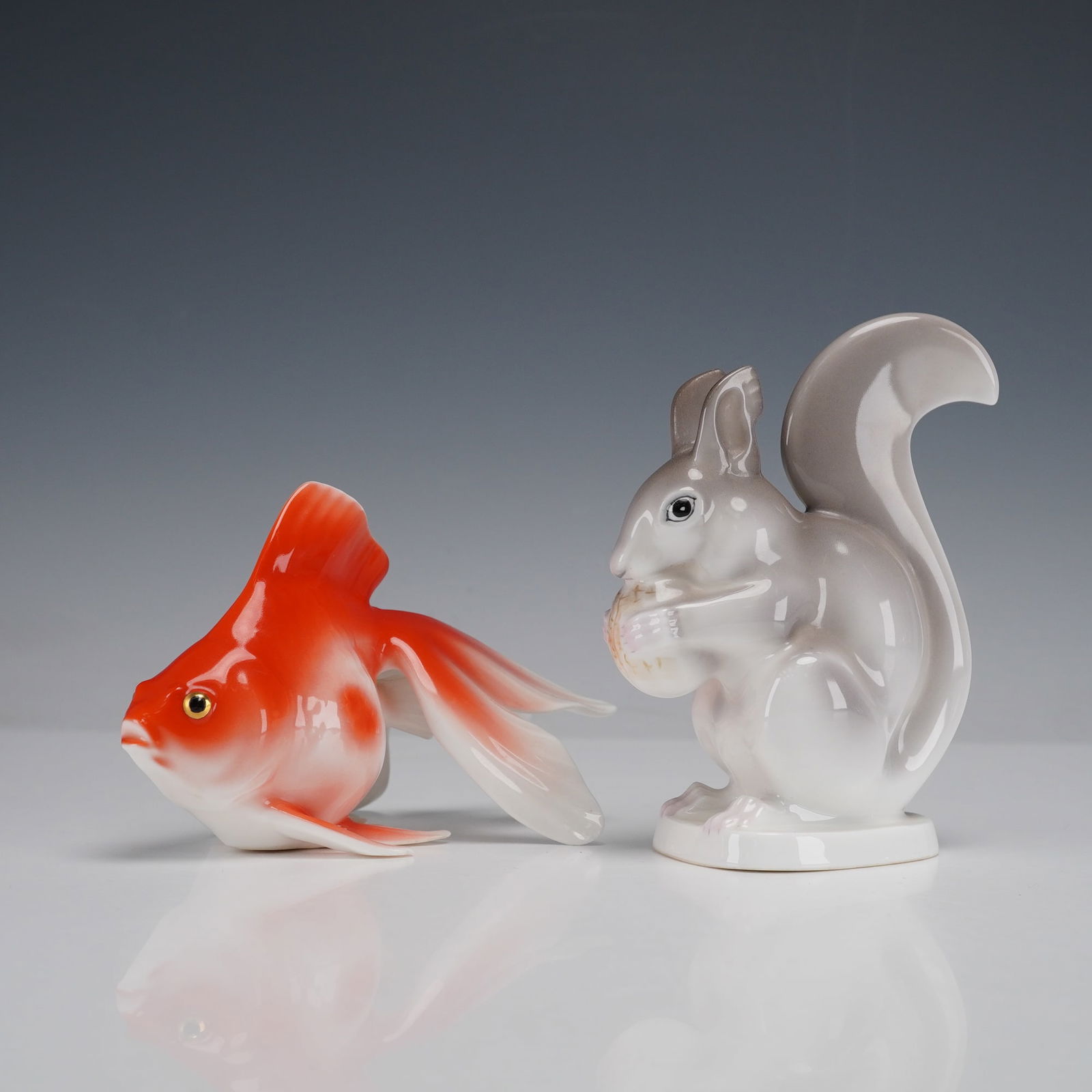 Pair of Noritake Squirrel and Goldfish Figurines: A pair of glazed porcelain figurines: a white/gray squirrel holding a nut and a red'orange/white goldfish with flowing fins. Both bear red and gold Noritake JAPAN backstamp. Dimensions: 6.00"L x 3.50"