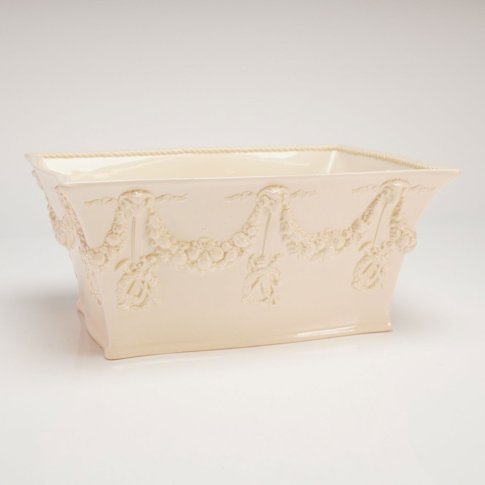 Wedgwood Embossed Queensware Planter: A rectangular ceramic container executed in Wedgwood Embossed Queen's Ware, finished with a cream-colored glaze, exhibiting a Neoclassical style. The exterior features extensive relief molded decorati