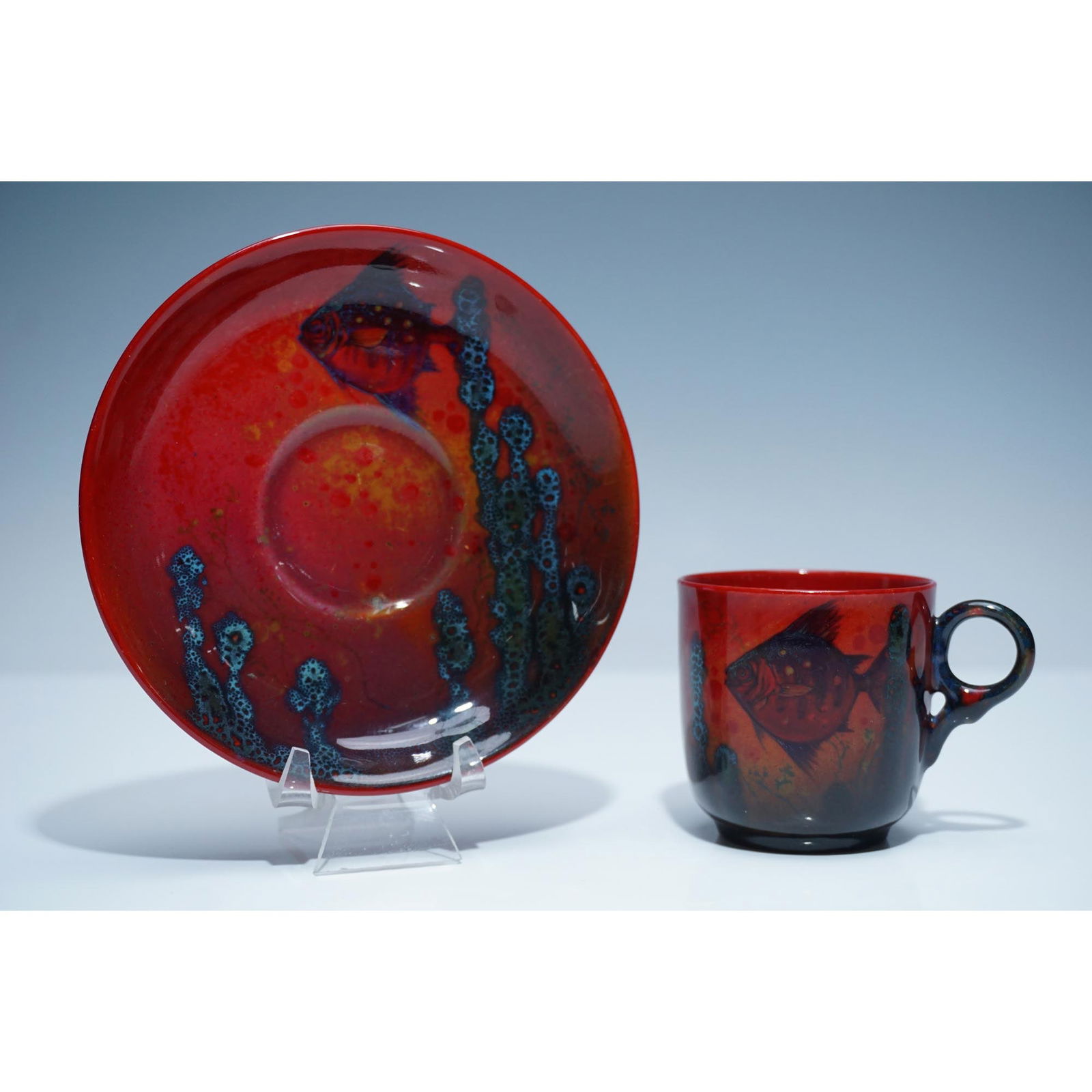 Royal Doulton Rare Flambe Sung Cup & Saucer w/ Fish Design: This exceptional Royal Doulton Flambe Sung cup and saucer set showcases the renowned artistry of Royal Doulton with its rich flambe glaze and distinctive fish design. The cup features an elegant red a