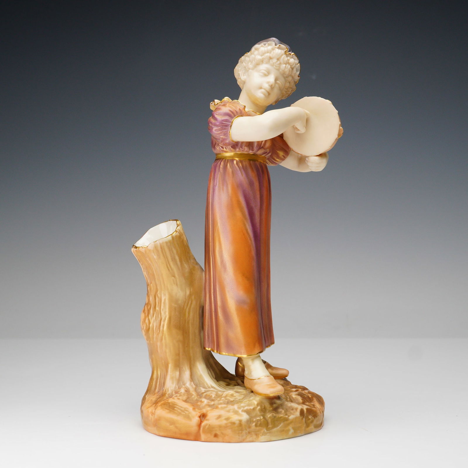 Royal Worcester by James Hadley Boy with Tambourine Spill Vase: An exquisite Royal Worcester porcelain spill vase modeled by James Hadley, depicting a young boy playing a tambourine beside a hollow tree stump. Hand-painted in warm hues of plum, gold, and cream. Th