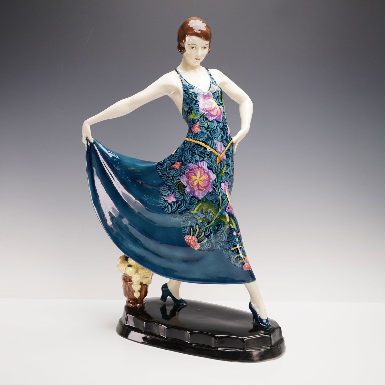 Goldscheider by Stefan Dakon Porcelain Art Deco Figurine: A striking Art Deco porcelain figure by Goldscheider Wien, modeled by Stefan Dakon. The piece depicts a stylish woman in a flowing blue dress with vibrant hand-painted floral decoration, posed gracefu