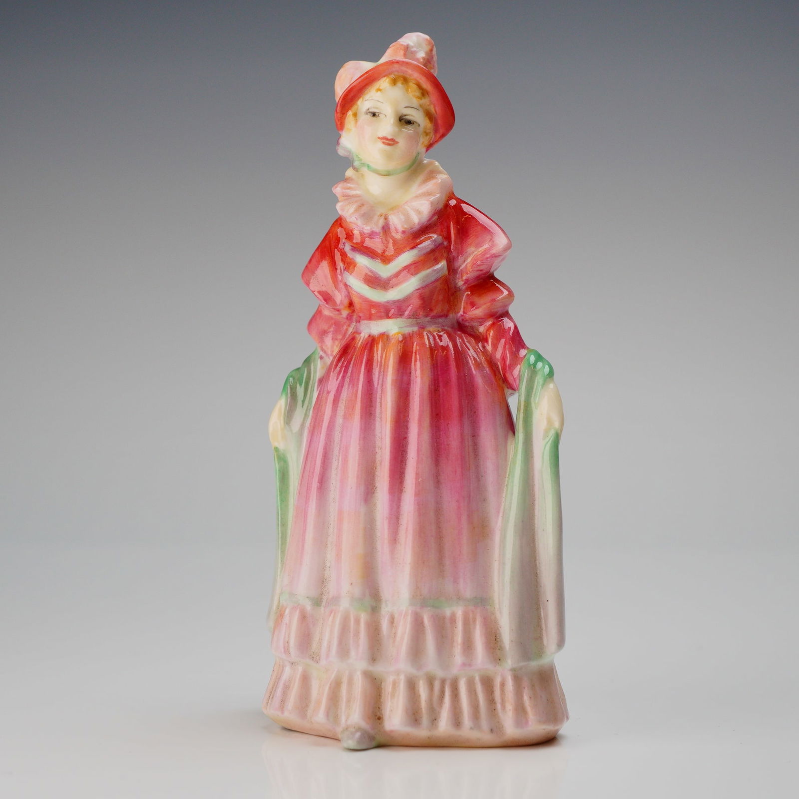 Royal Doulton Miniature Figurine, Norma M36: A single glazed ceramic figurine, identified as Royal Doulton model Norma, M36. The miniature figurine depicts a standing woman dressed in an elaborate, full-skirted period costume, characterized by a