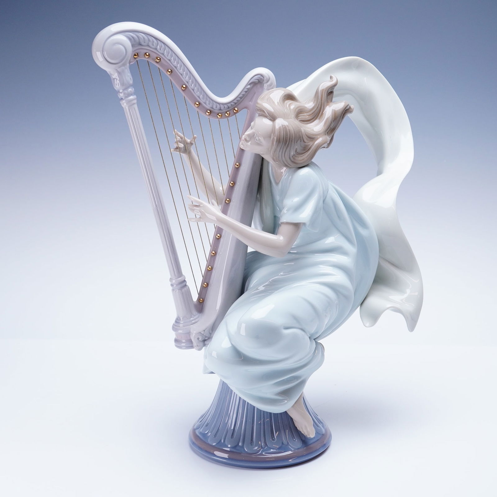 Lladro Porcelain Sculpture The Harpist 1006312: Sculpture depicts a floating female figure playing a harp. This handcrafted Spanish porcelain art piece is rendered in a glossy finish, featuring a figure dressed in a pale blue/aqua gown with
