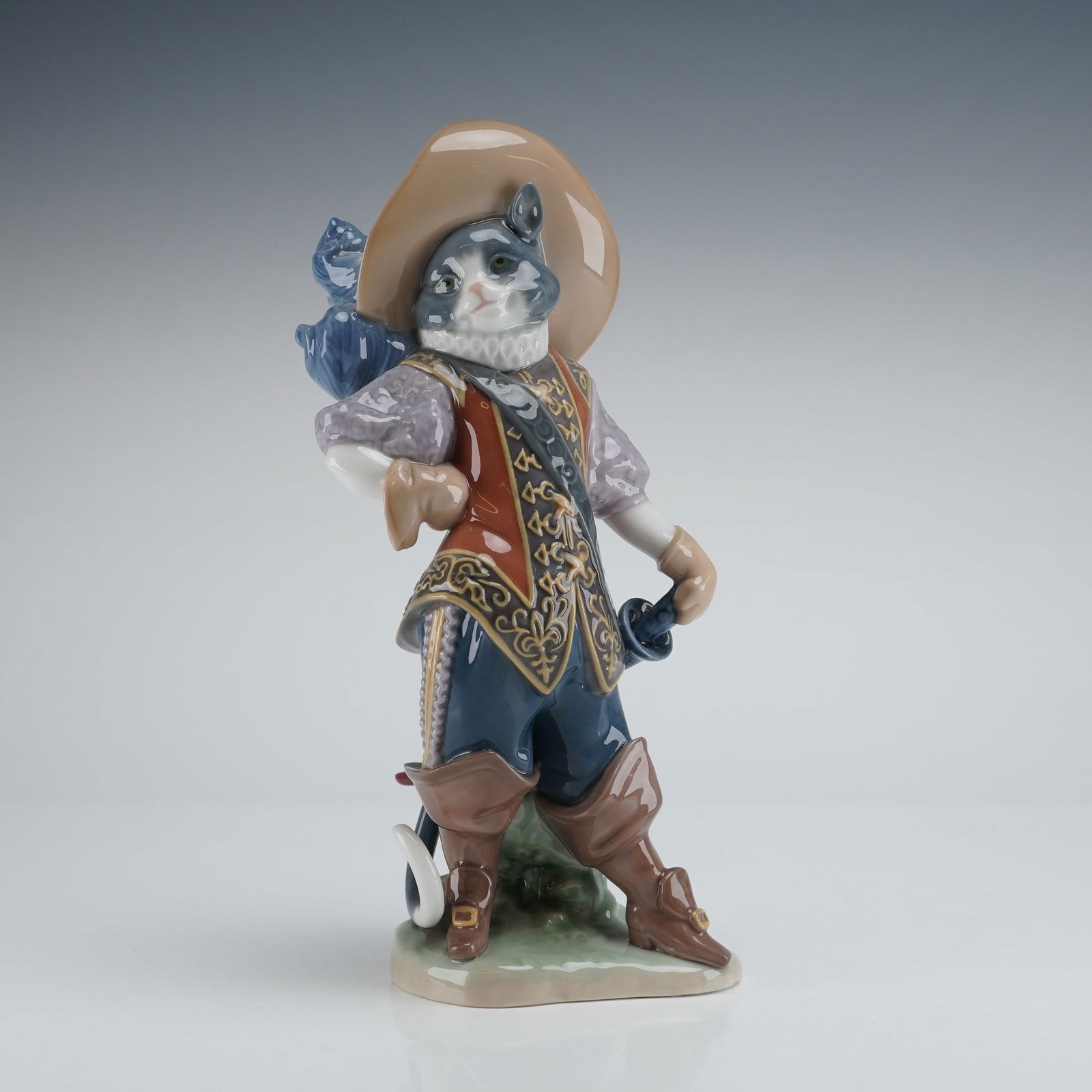 Lladro Puss in Boots Figurine 8599: A Lladro porcelain figurine depicting the character Puss In Boots, a figure from European folklore. The anthropomorphic cat is dynamically posed as a 17th-century cavalier or musketeer, wearing a