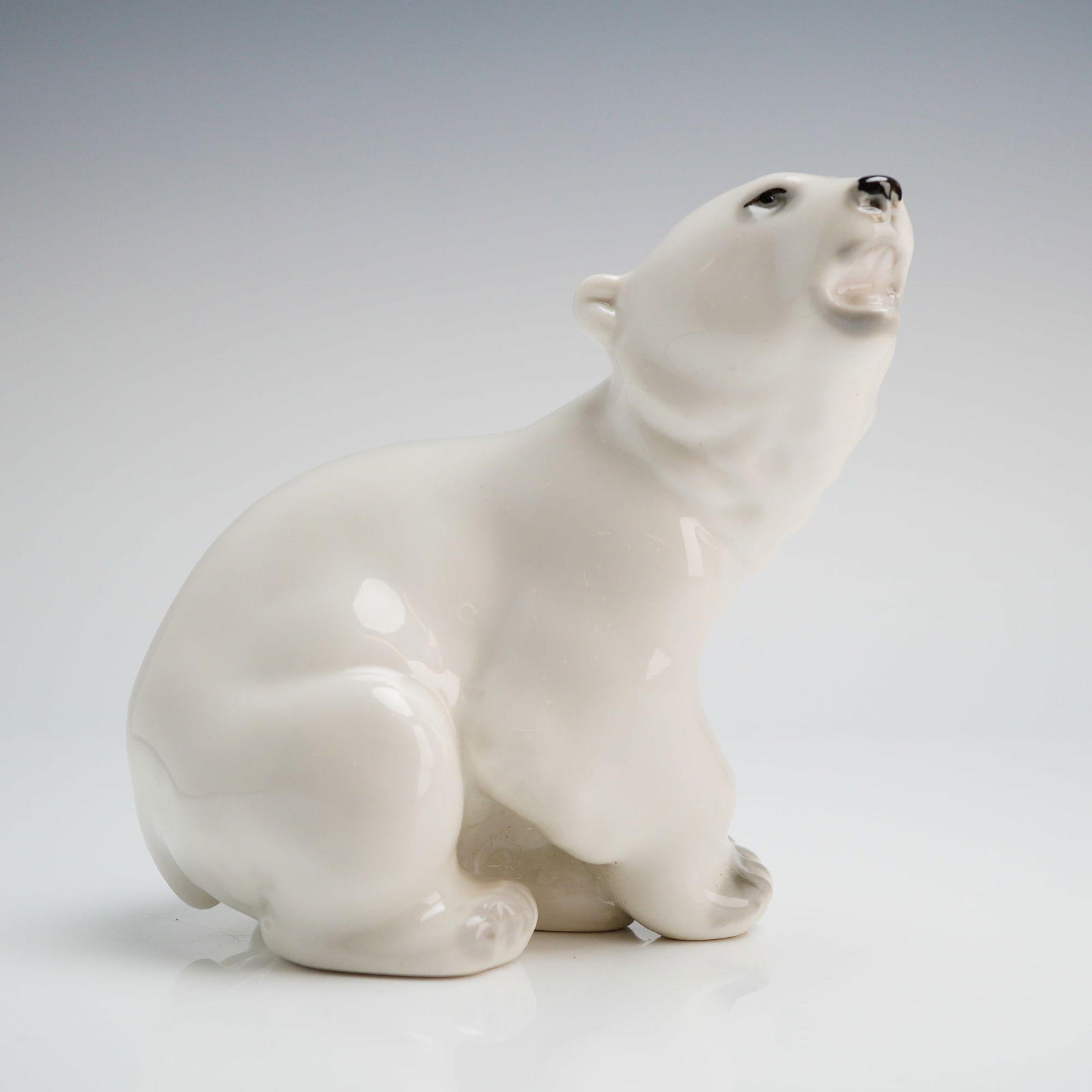 Lomonosov Porcelain Figurine of a Polar Bear Cub: A porcelain figurine attributed to the Lomonosov Porcelain Factory (LFZ). The piece depicts a single seated polar bear cub looking upward with its mouth open, rendered in a naturalistic style. The