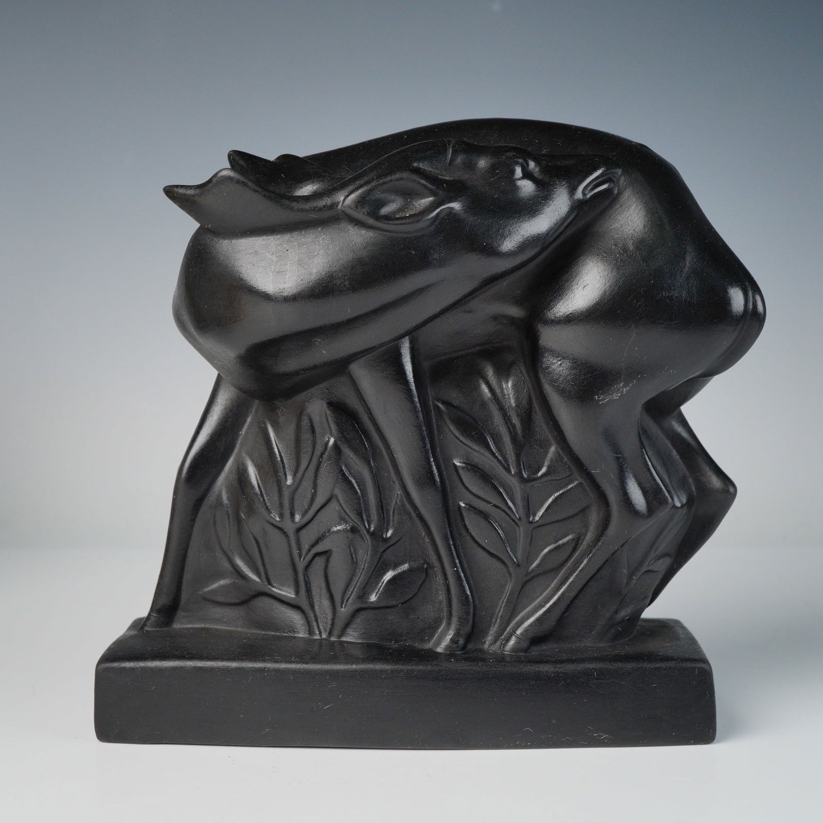 Wedgwood by John Skeaping Art Deco Black Basalt Deer Figurine: A stylized ceramic figure designed by John Skeaping for Wedgwood, modeled as a recumbent deer set on a rectangular plinth. Executed in uniform black basalt, the background is embellished with