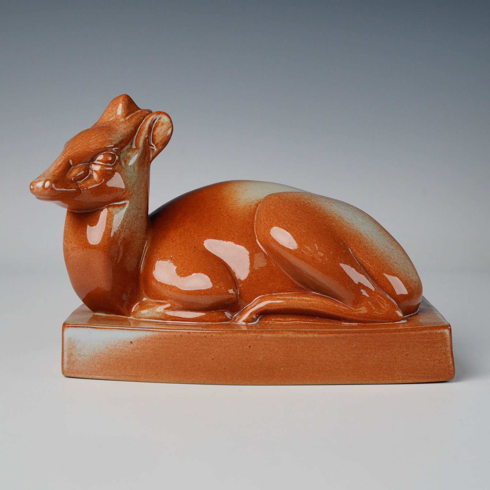 Wedgwood by John Skeaping Brown Glazed Ceramic Art Deco Deer Figurine: An Art Deco ceramic sculpture by John Skeaping for Wedgwood, portraying a recumbent deer atop a rectangular plinth. The figure is finished in a glossy variegated glaze, dominated by rich rust-orange