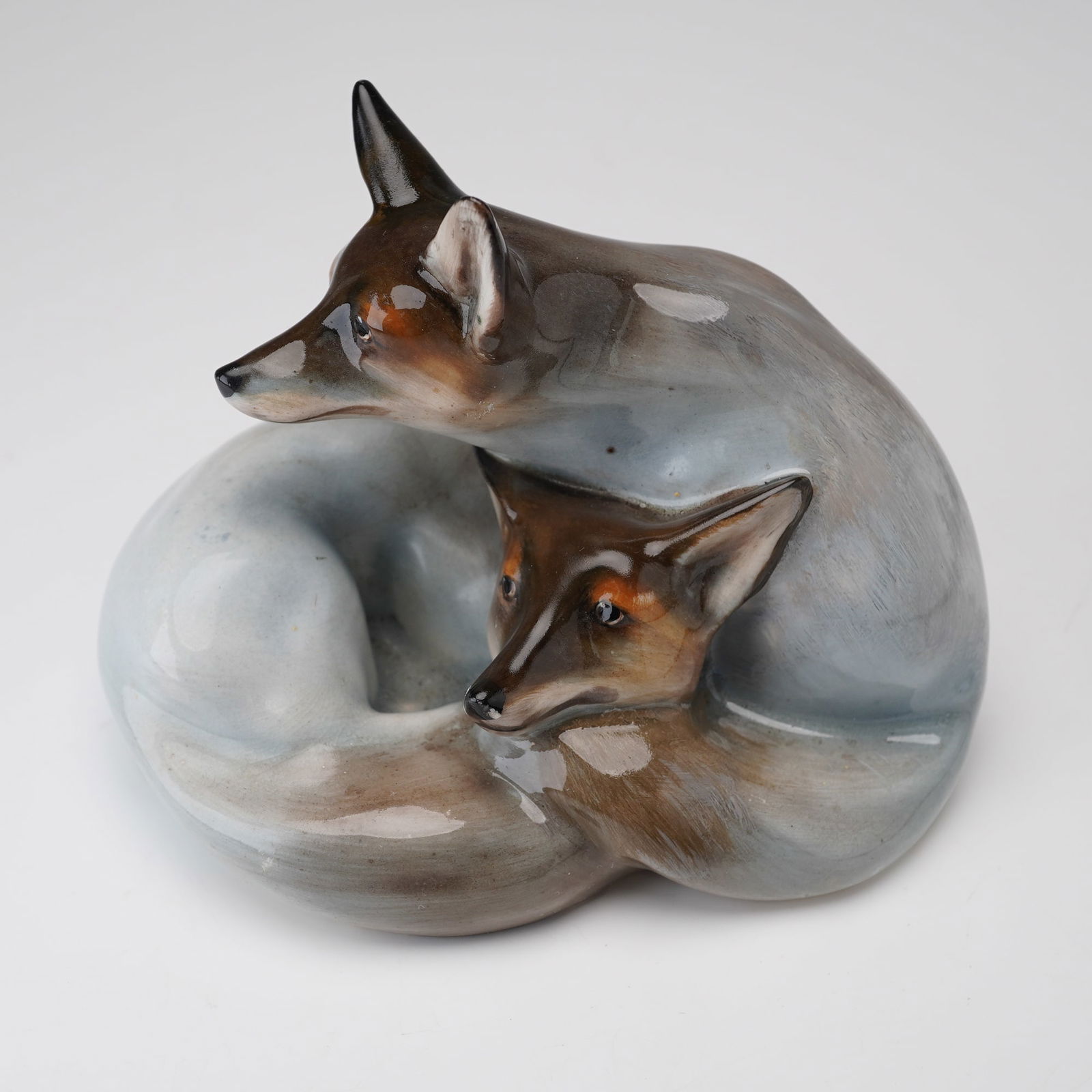 Royal Doulton Figurine, Foxes Curled HN117: Hand decorated and hand painted in a grey, light brown colorway. Two foxes nestled together in a resting pose. Handwritten HN number. Royal Doulton backstamp. Dimensions: 3"L x 4.75"W x 3.5"H