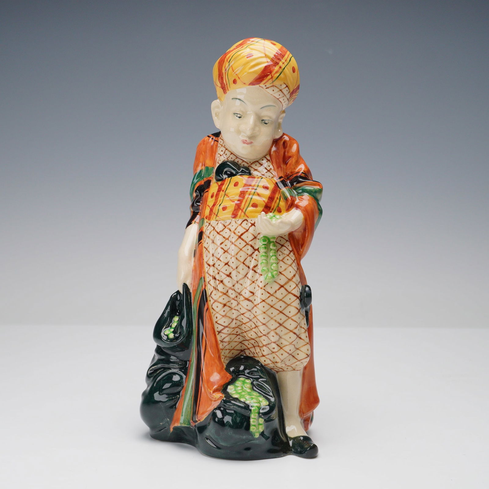 Rare Royal Doulton Colorway Figurine, One of the Forty: Royal Doulton figurine titled One of the Forty, first version, showing a figure wearing a patterned turban and robe while holding strings of green beads. This is a colorway example featuring an orange