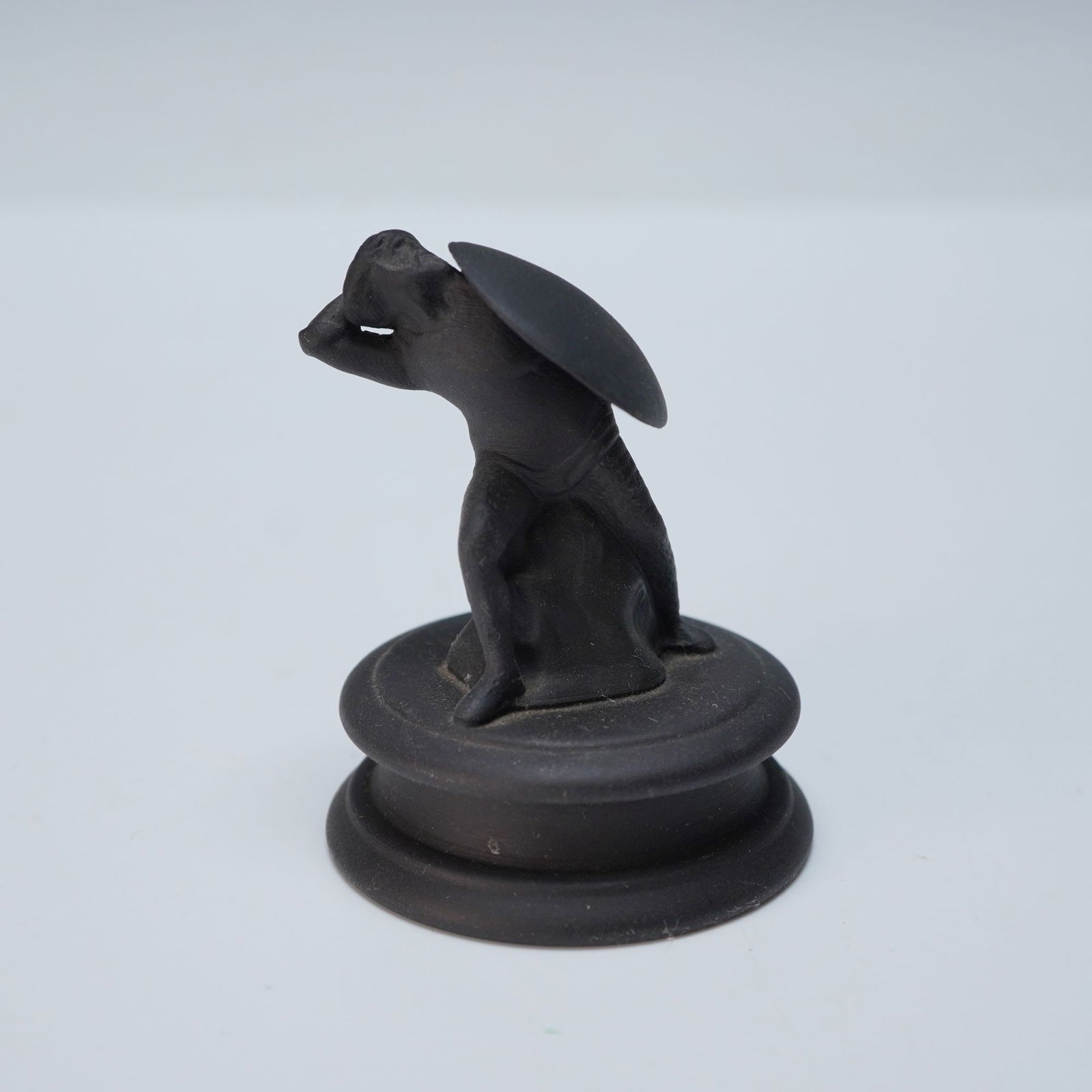 Wedgwood by John Flaxman Black Basalt Chess Piece, Pawn: A Wedgwood Basalt Ware figure depicting a crouching classical-style figure with an arm raised to the head and a shield on its back, mounted on an integral circular plinth base. Crafted from unglazed m