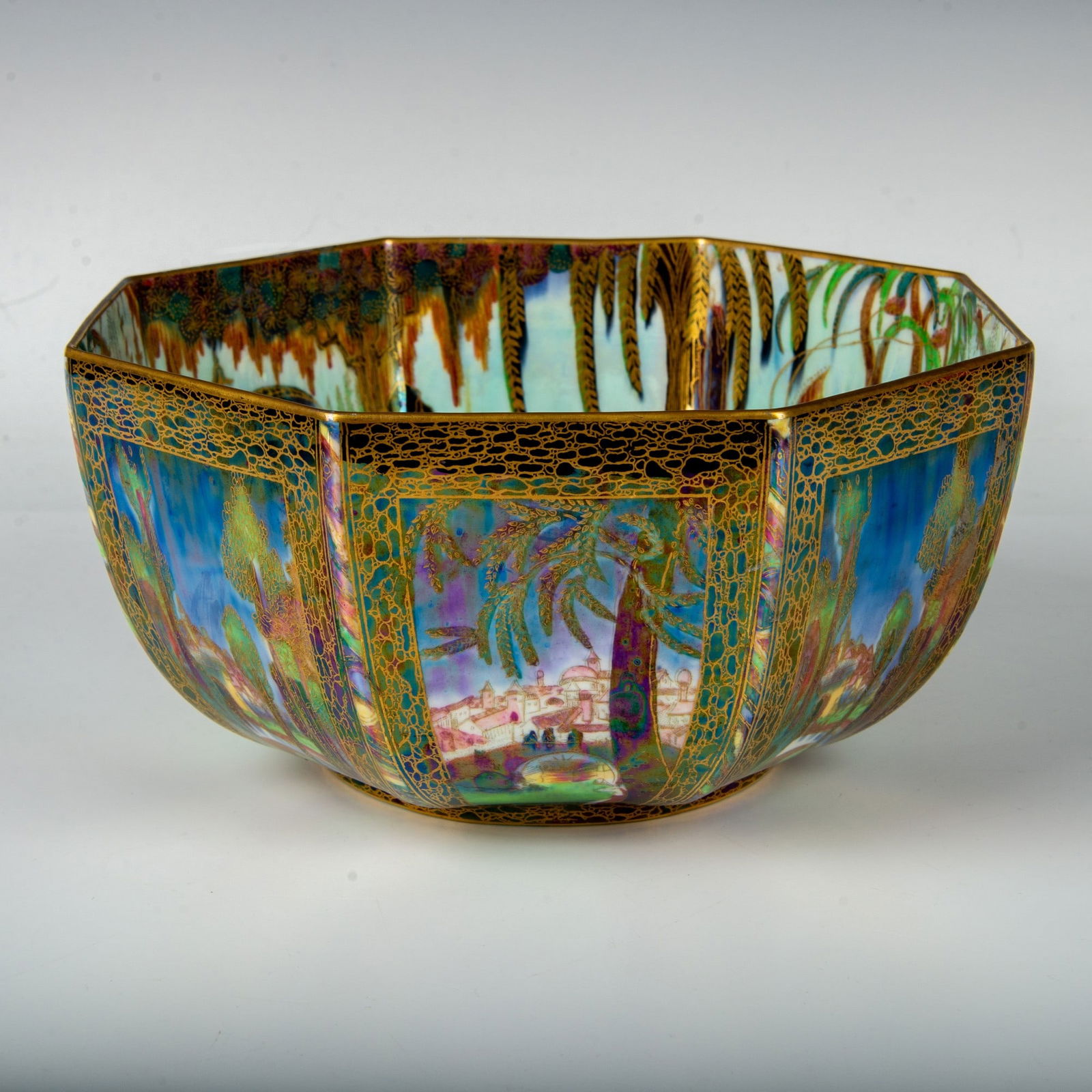 Wedgwood Fairyland Lustre Bowl, Dana - Castle On a Road: Z5125; a beautiful octagon-shaped bowl depicting Dana - Castle On a Road on the exterior; blue sky, pink rooftops and black trees with green foliage. The interior is decorated in the Fairy In a Cage p