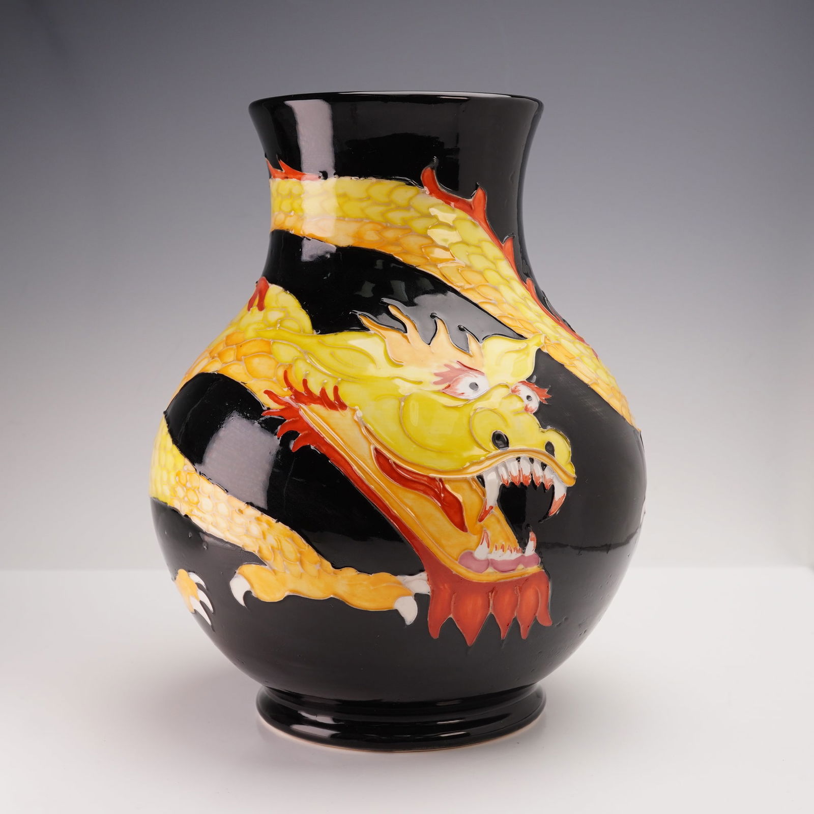 Moorcroft Pottery by William John Moorcroft Trial Dragon Vase: Exceptional pottery vase featuring a striking decoration of a coiled dragon wrapping completely around. This tube lined dragon designed in vibrant red, orange, and yellow hues and set against a black