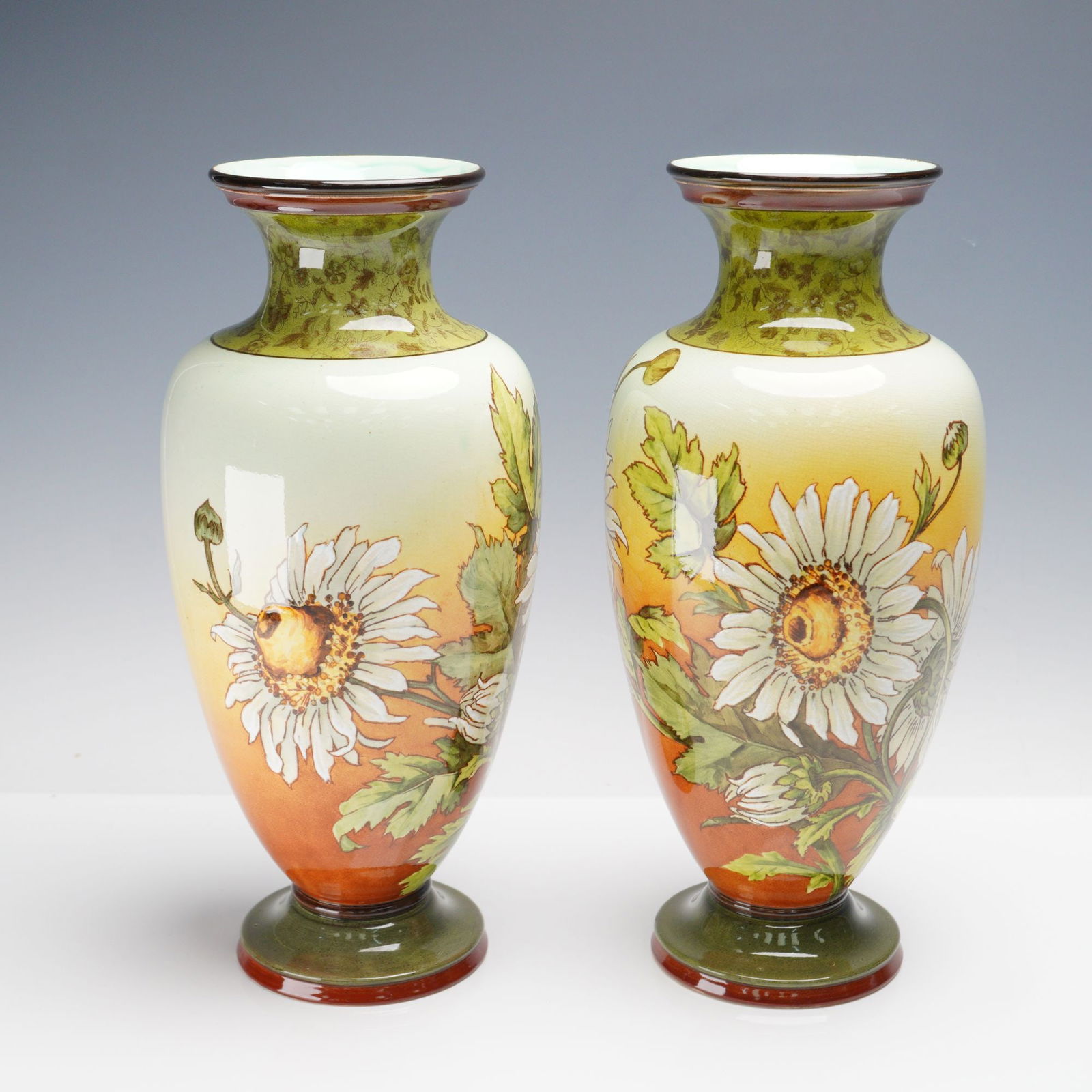 Pair of Doulton Lambeth Faience Vases, White Daisies on Yellow Background: This pair of Doulton Lambeth vases features white daisies on a yellow, green, and light brown background, with a floral band around the neck. The baluster-shaped vases have a celadon glazed interior
